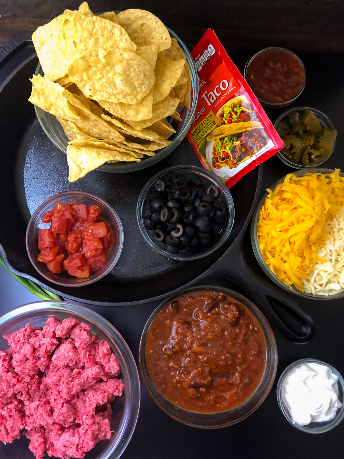 Ingredients for cast iron skillet nachos including ground beef tortilla chips cheese and toppings