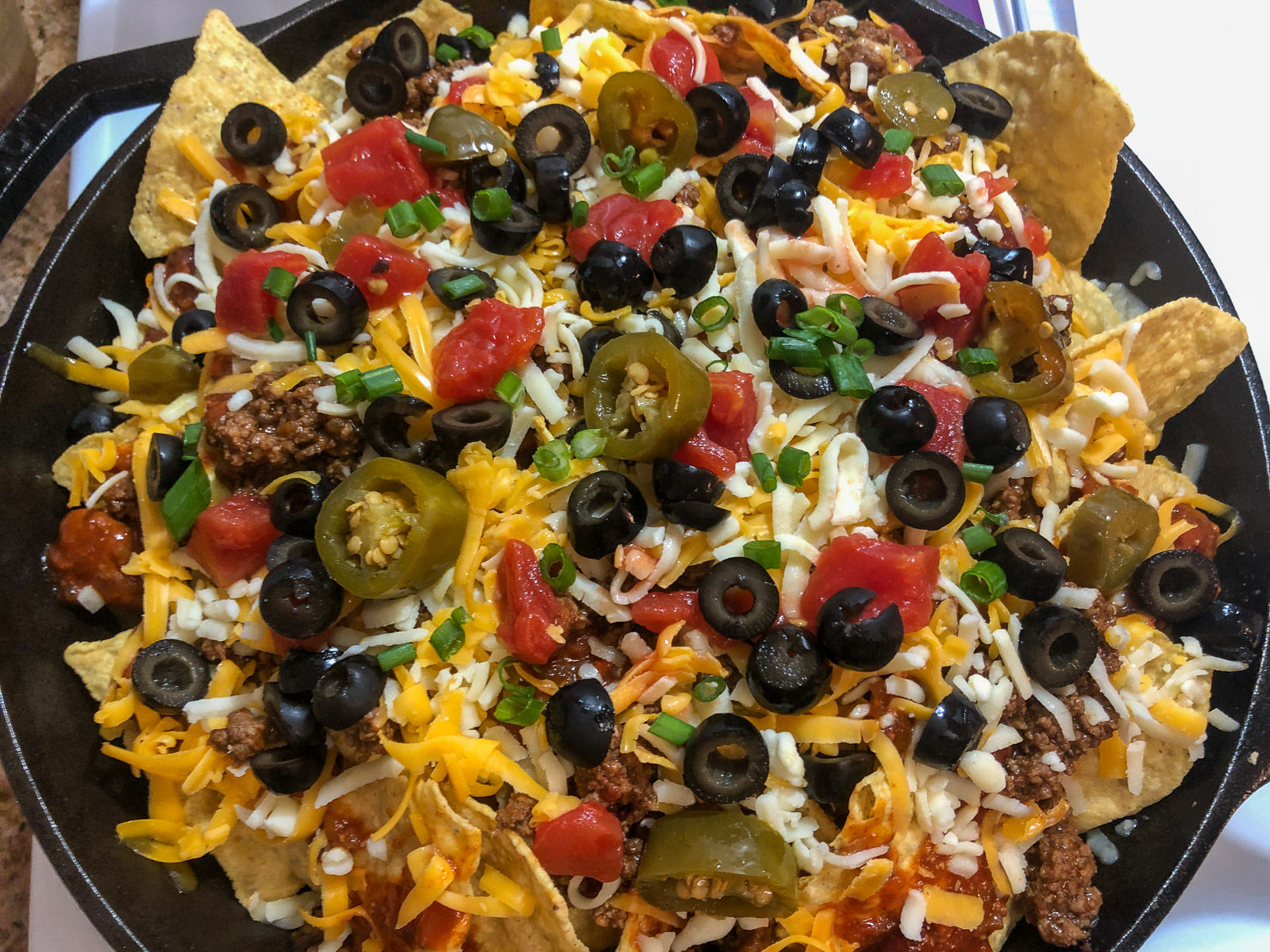 Fully assembled loaded cast iron skillet nachos ready to bake with cheese and toppings