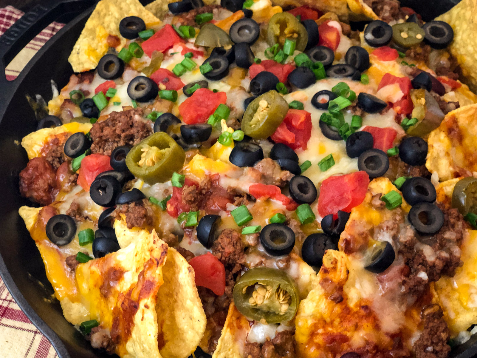Finished cast iron skillet nachos with melted cheese and loaded toppings fresh from the oven