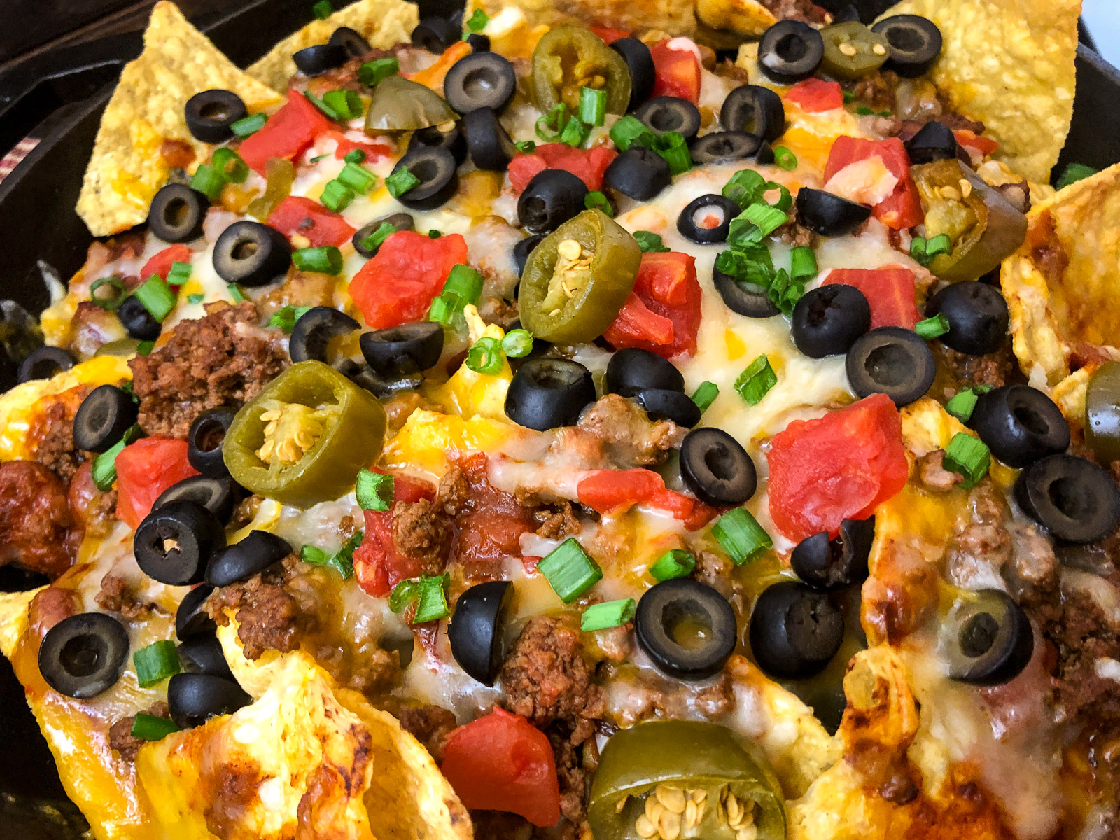 Side view of loaded cast iron skillet nachos with sour cream and salsa
