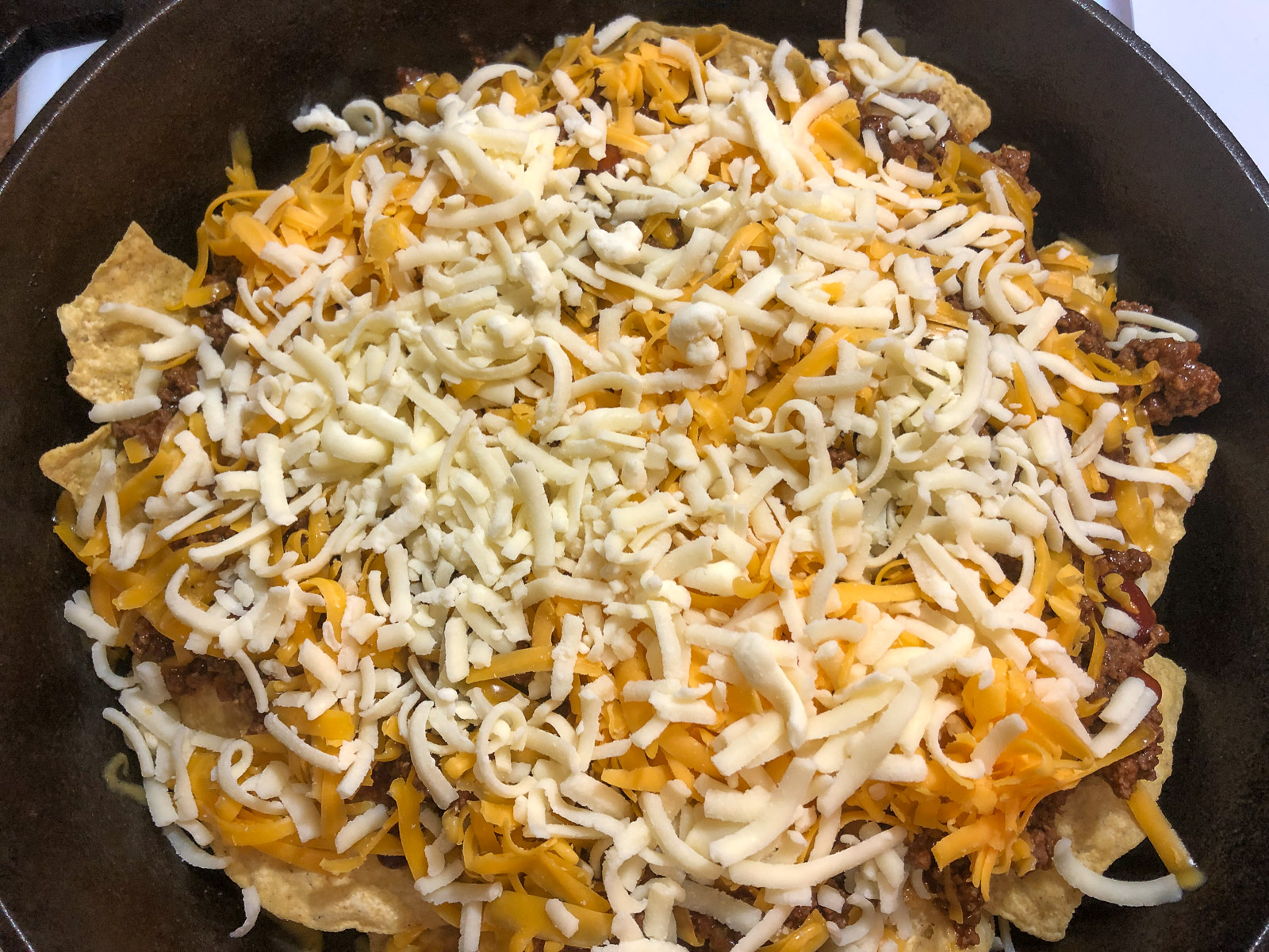 Corn tortilla chips layered in a cast iron skillet topped with chili taco meat and cheese for cast iron skillet nachos