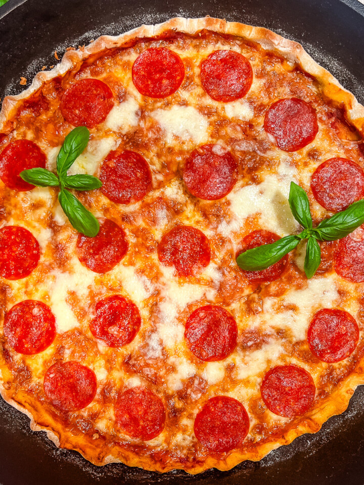 A cast iron pizza garnished with fresh basil.