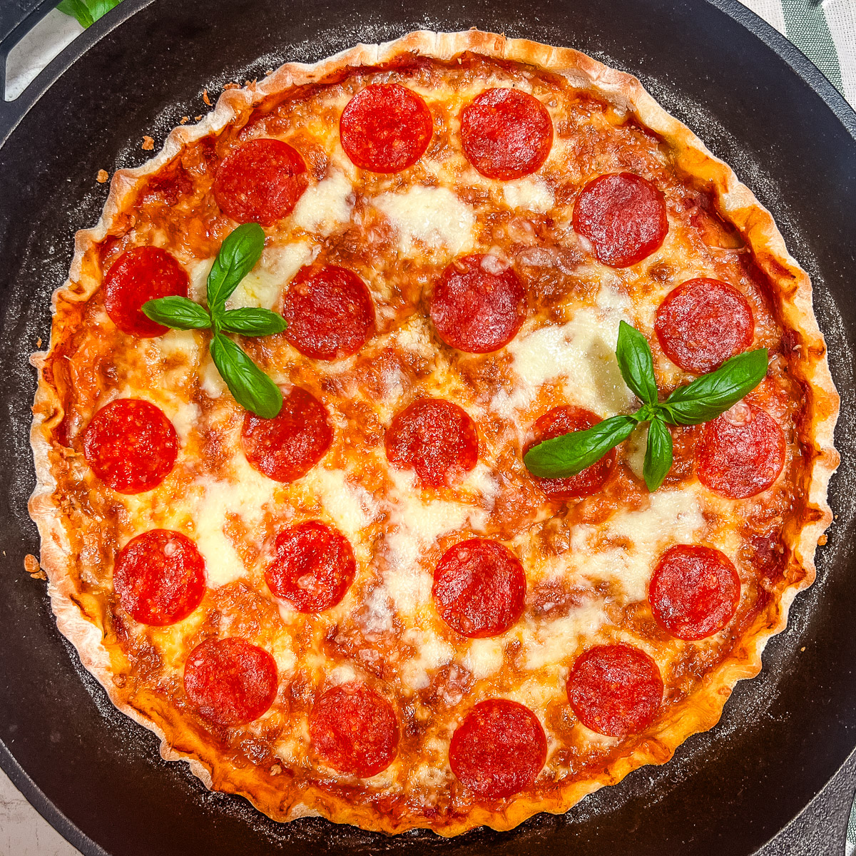 A cast iron pizza garnished with fresh basil.