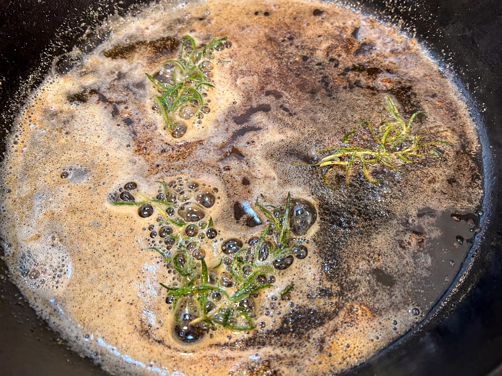 4 cooked New York strip steaks in a cast iron skillet garnished with fresh rosemary.