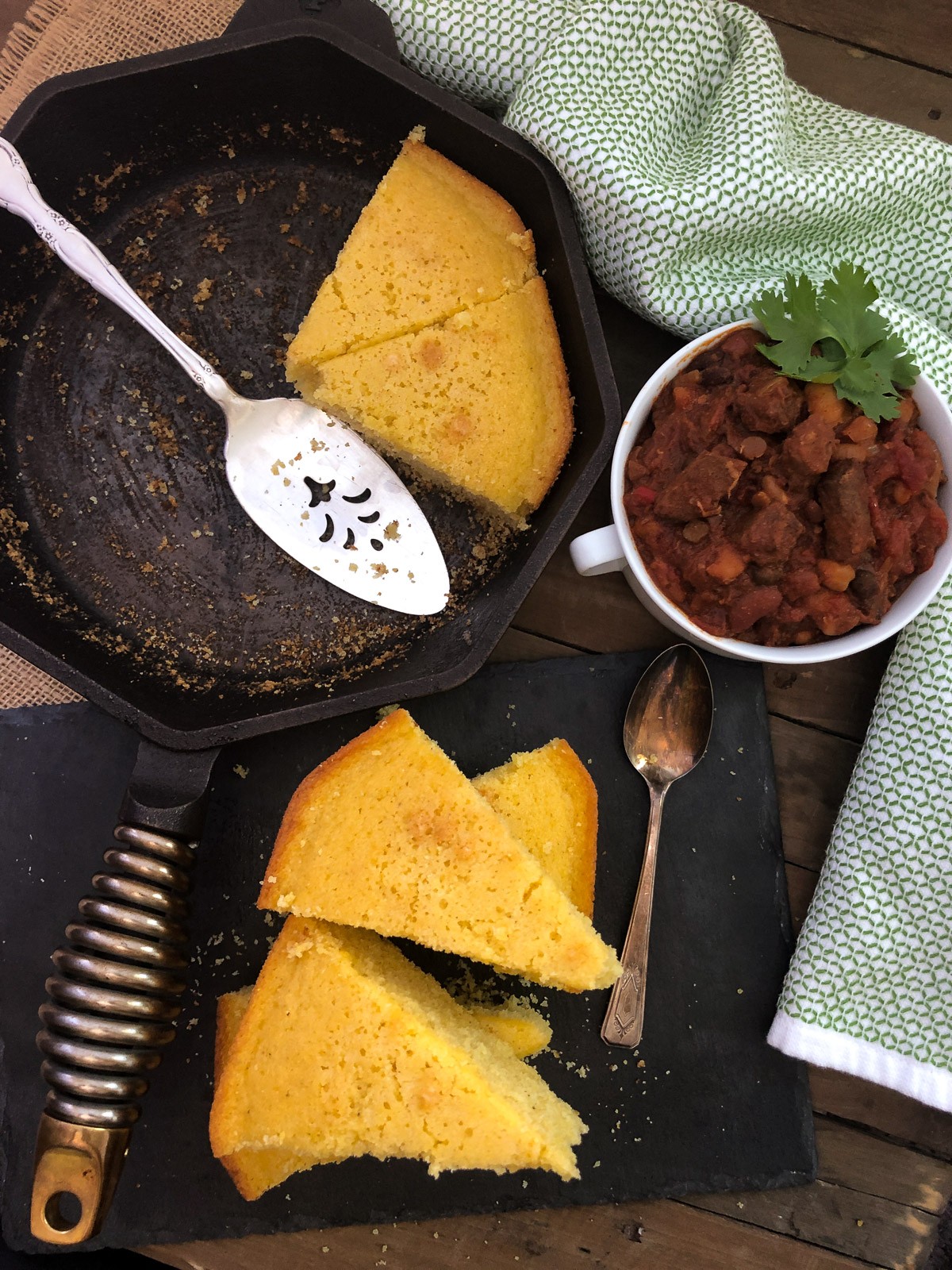 Sweet Cornbread sliced, partially on a platter and in the skillet with a side of chili. 