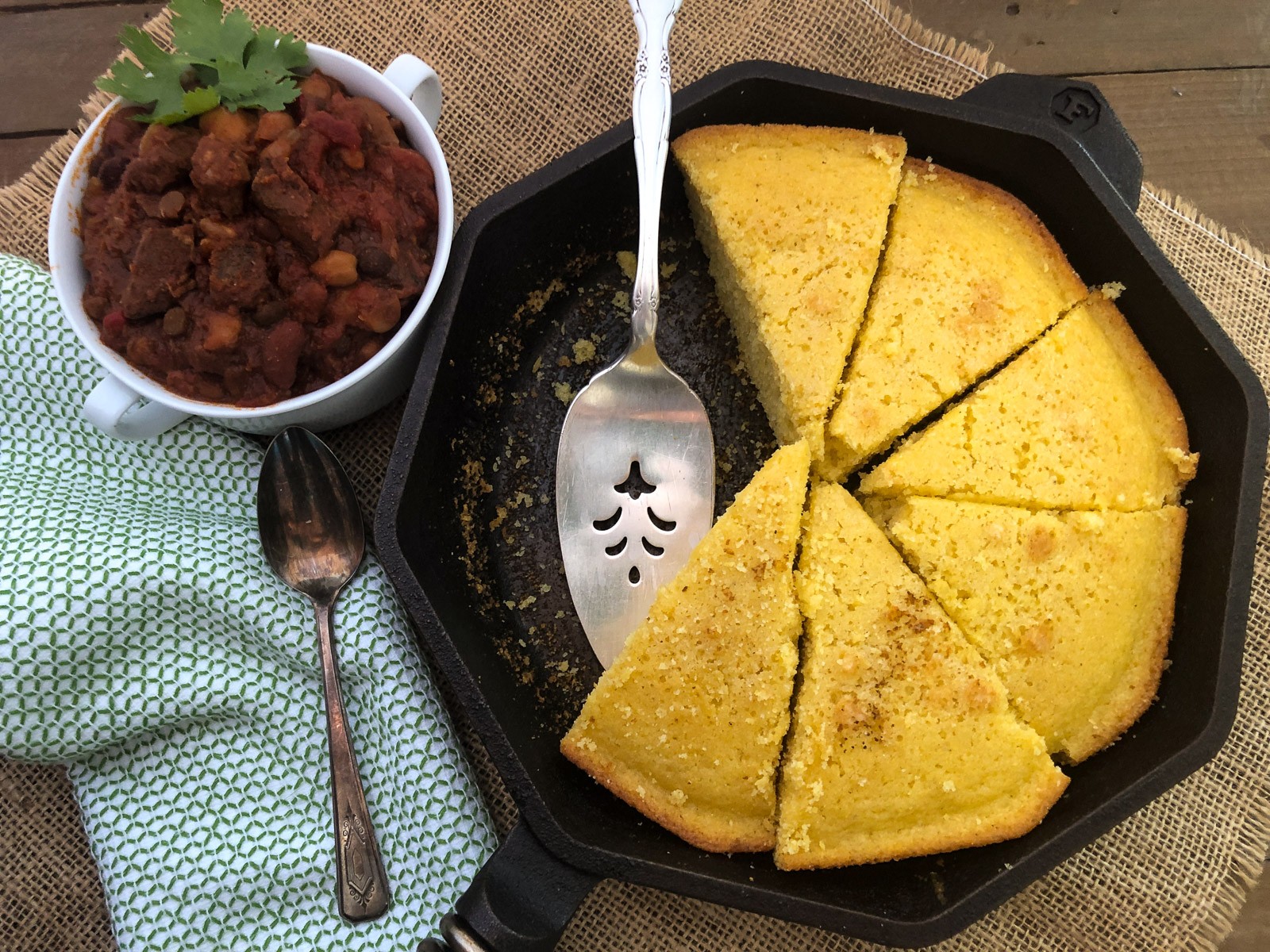 Sliced sweet cornbread in a skillet with a cup of chili.