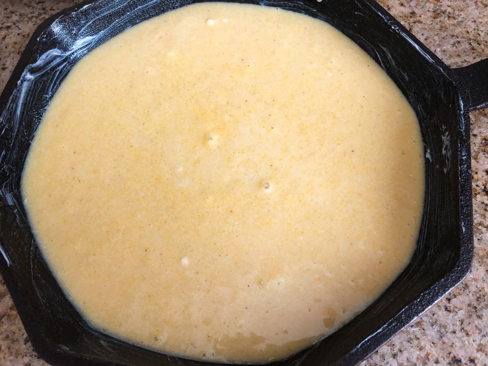 The sweet cornbread batter has been poured the prepared cast iron skillet.