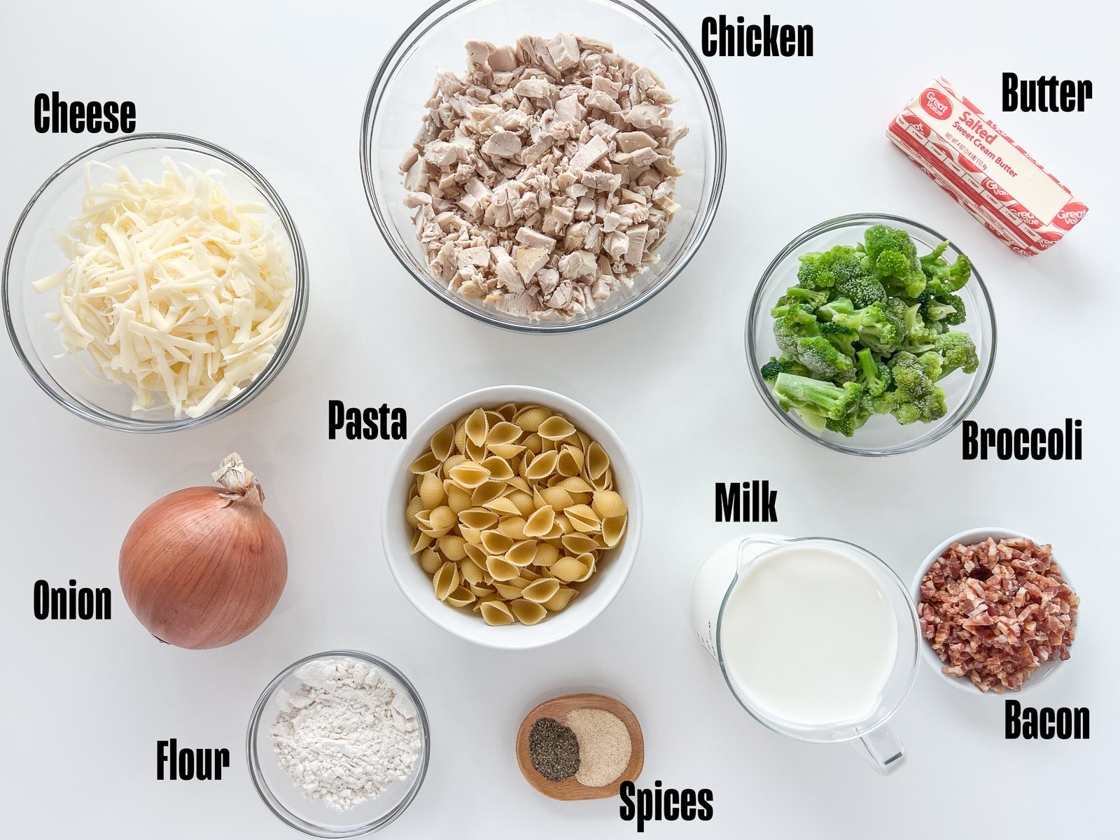 Ingredients to make chicken broccoli casserole: mozzarella cheese, rotisserie chicken, butter, broccoli, bacon, milk, granulated garlic, pepper, flour, shell pasta, and onion.