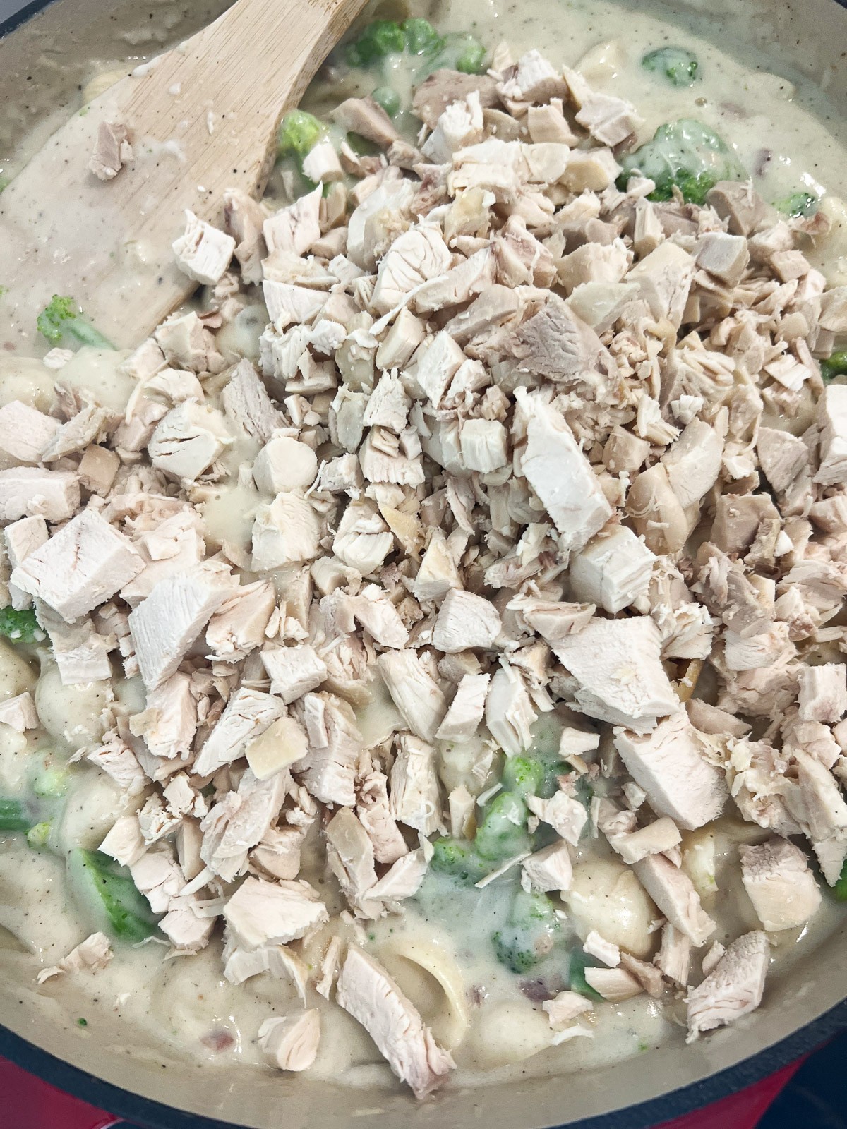 Chopped cooked chicken being stirred into the cheesy pasta with broccoli.