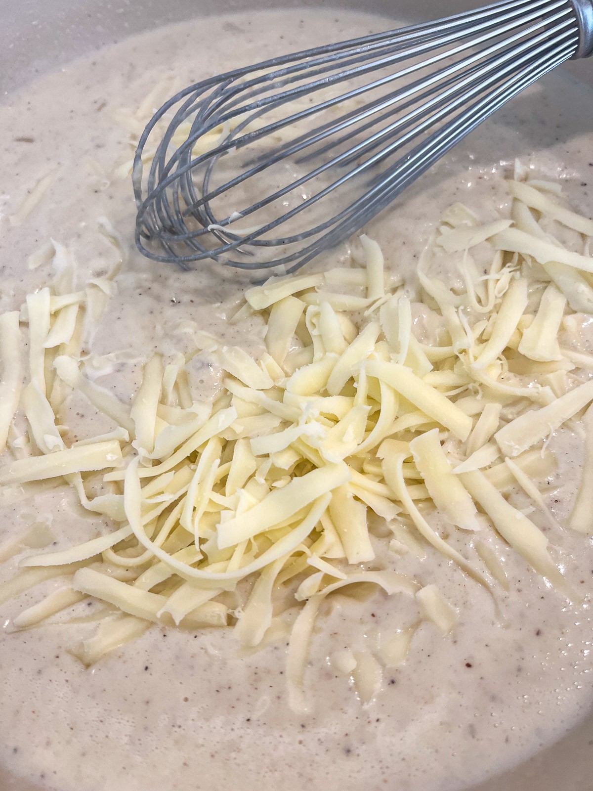 Shredded mozzarella cheese being incorporated to the cream sauce.