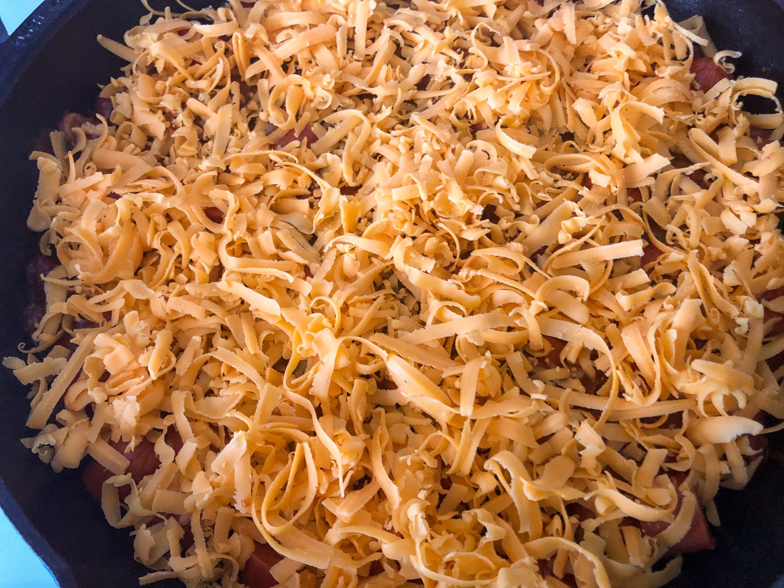 Sharp cheddar cheese covers the chili dog mixture in a cast iron skillet.
