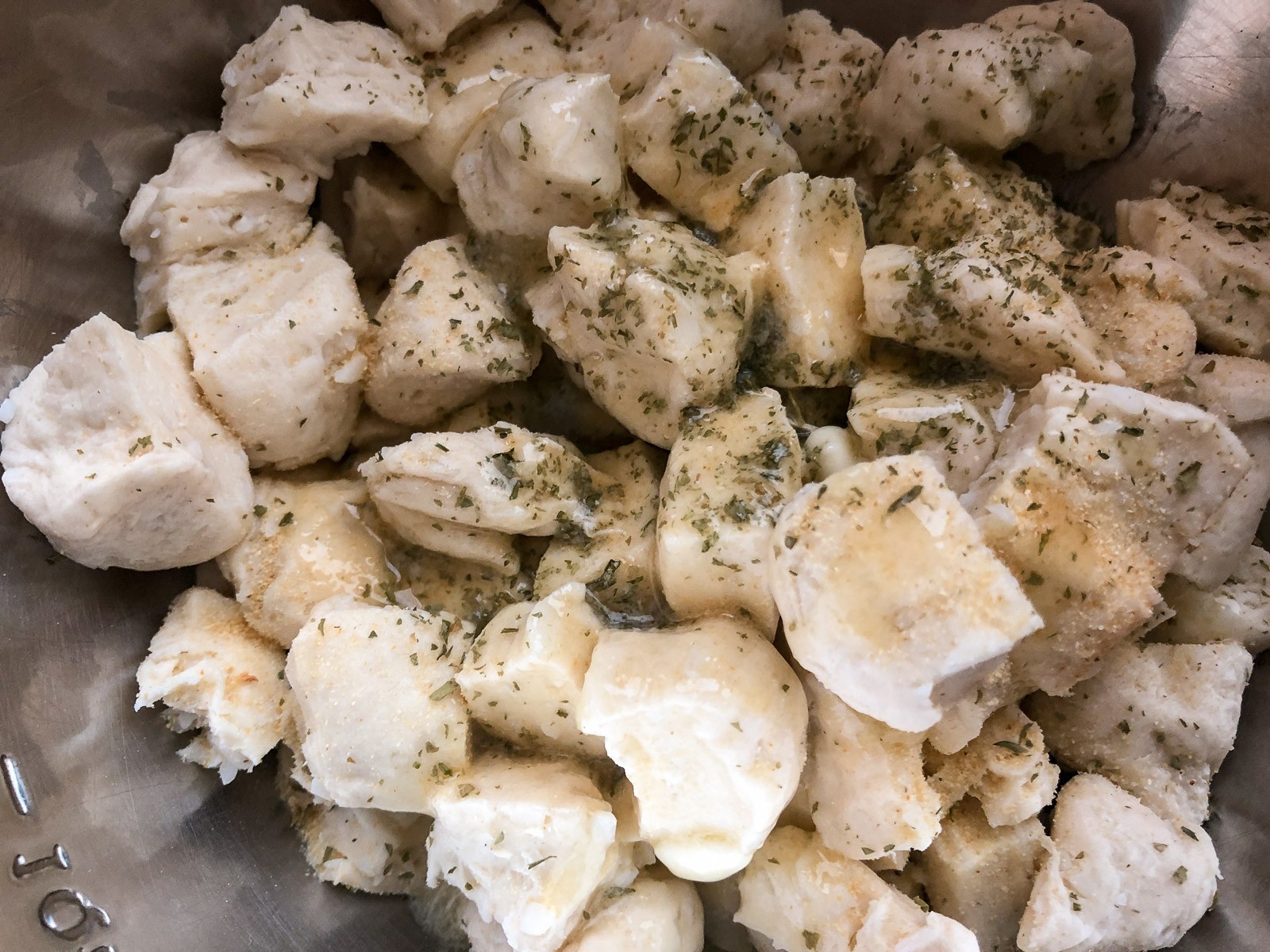 Canned biscuits tossed with melted butter, granulated garlic, and dried parsley in a stainless steel bowl.