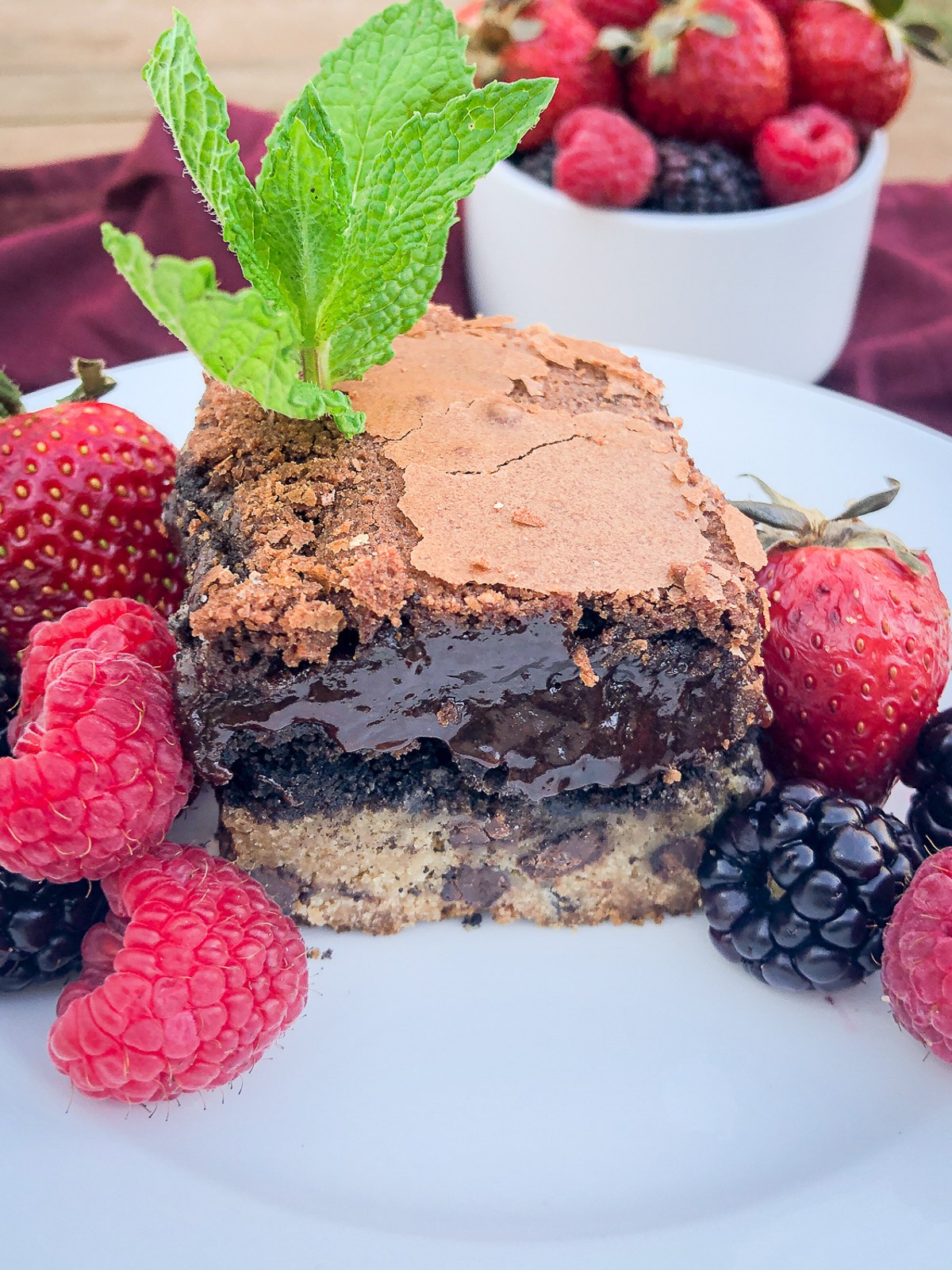 A square piece of Chocolate Chip Cookie Brownie on a white plate garnished with fresh mint and berries.