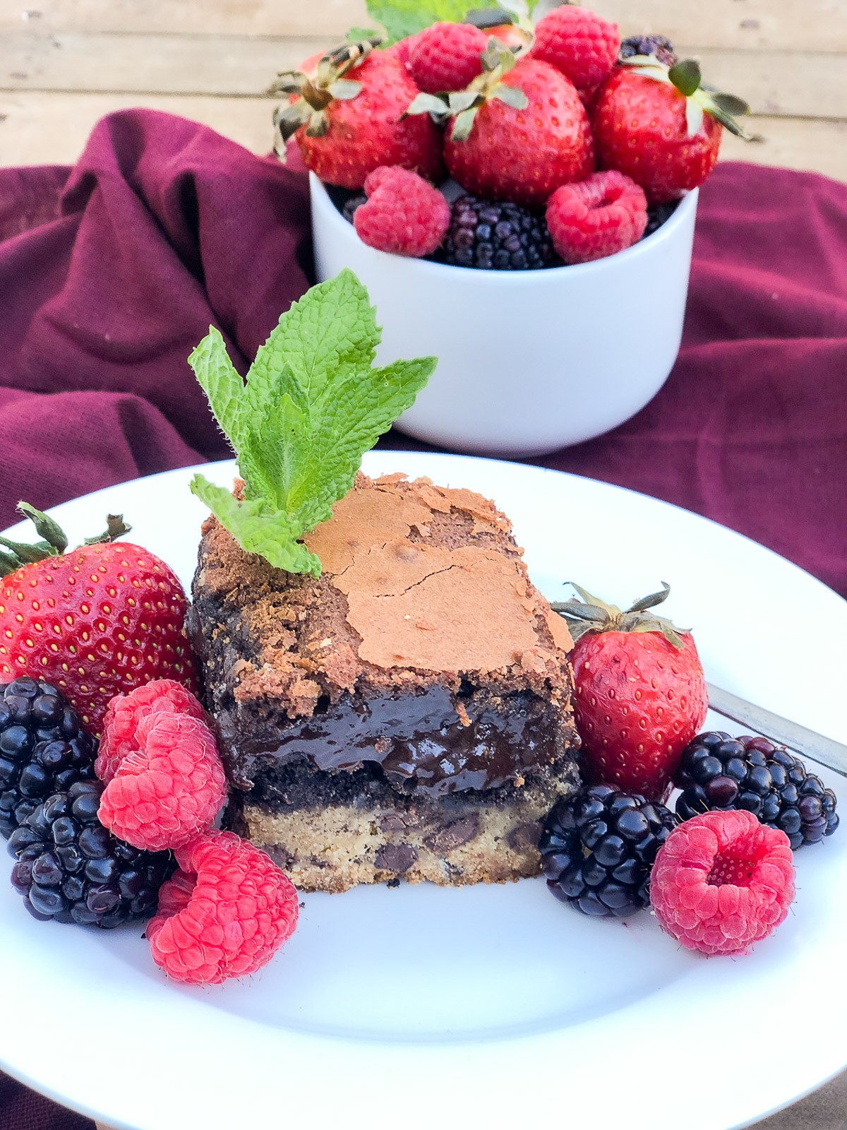 Chocolate chip cookie brownie on a white plate with a trio of berries.