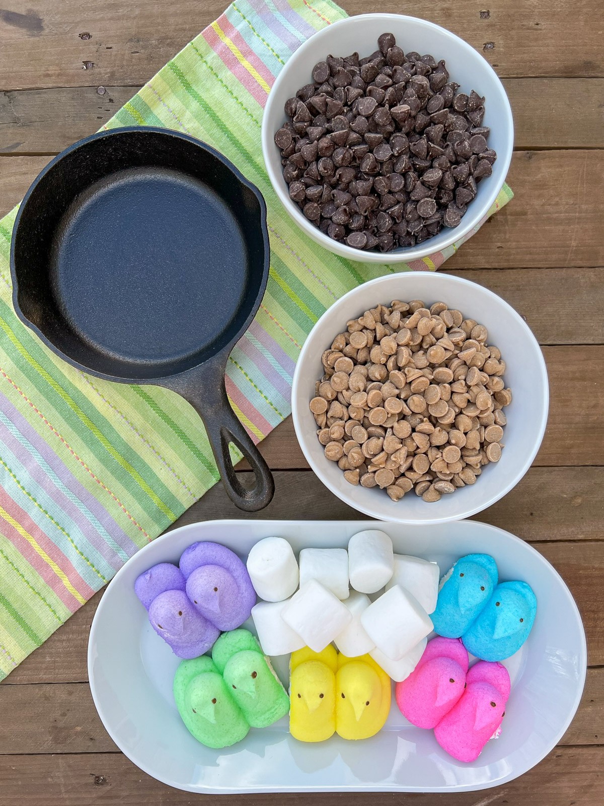 Ingredients for chocolate peanut butter dip: a cast iron skillet, chocolate chips, peanut butter chips, marshmallows, and Easter Peeps.