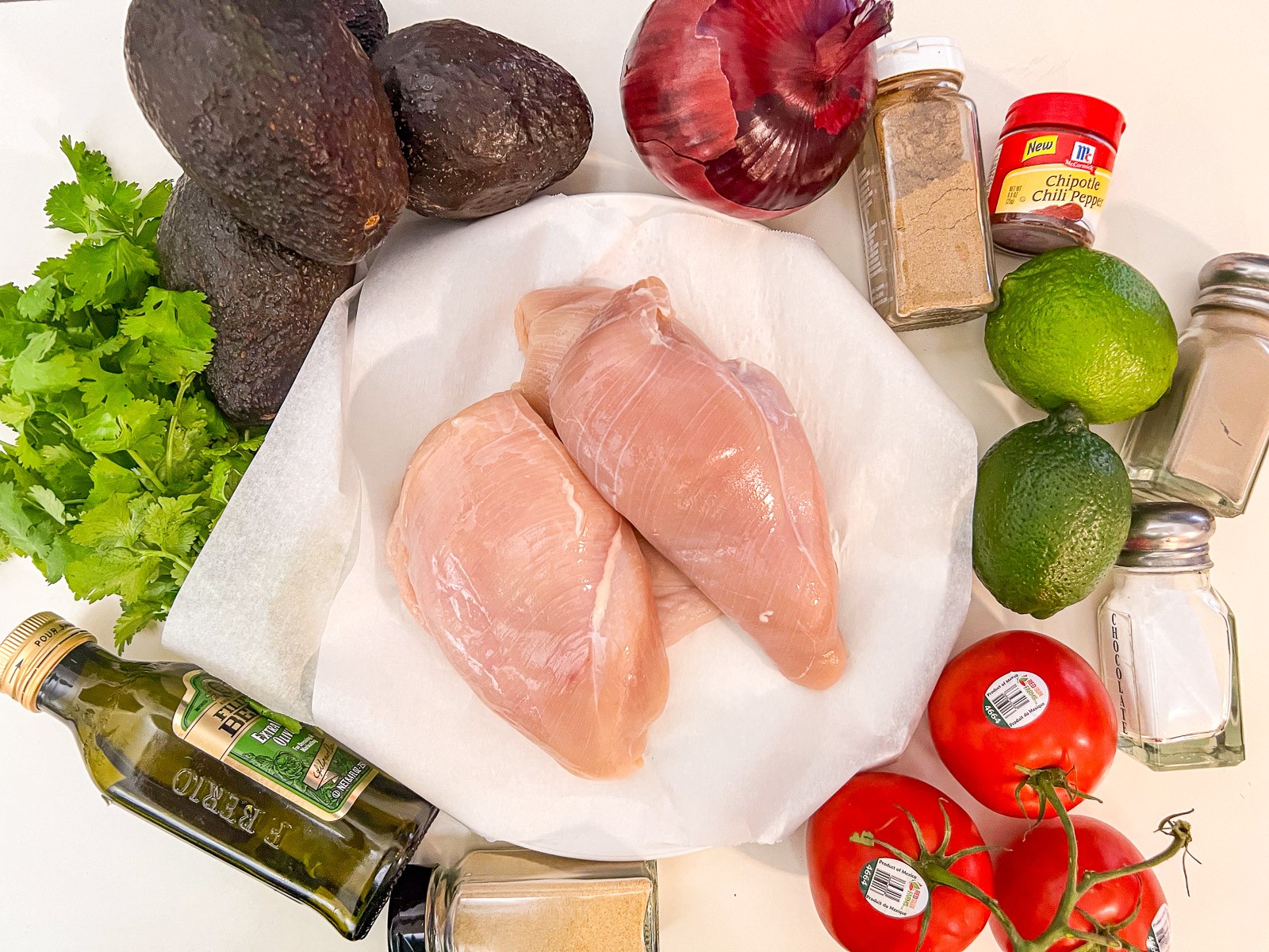 Ingredients to make cilantro lime chicken with avocado: avocados, red onion, cumin, chipotle powder, fresh limes, salt, pepper, tomatoes, granulated garlic, cilantro, and chicken.