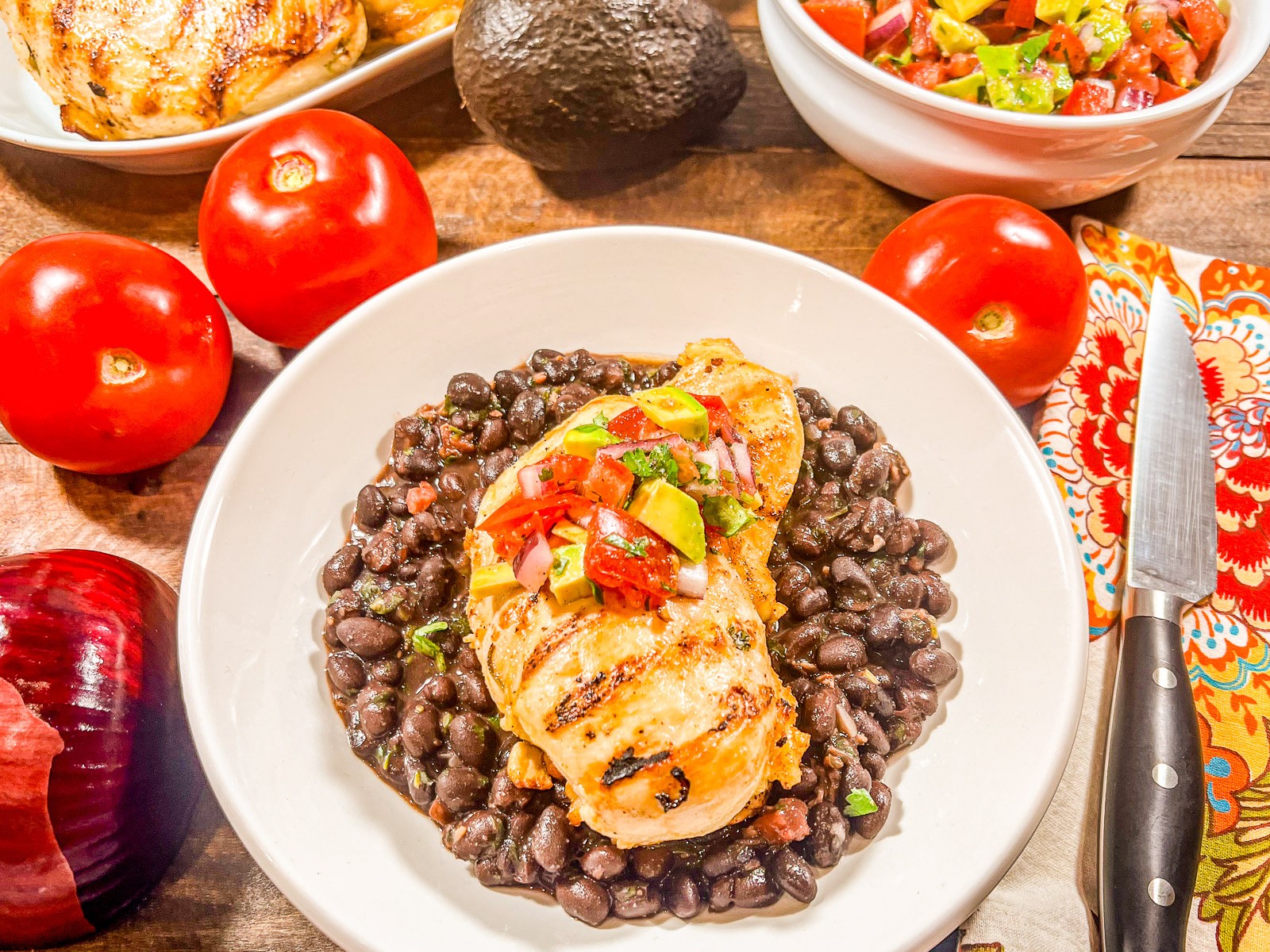 A piece of cilantro lime chicken resting in a bed of black beans topped with avocado salsa.