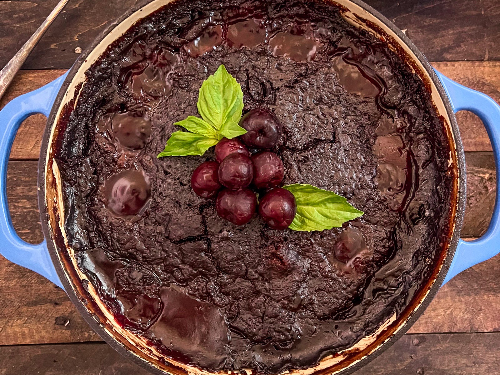Cola Chocolate Cherry Cake in a dutch oven garnished with fresh cherries and mint leaves.