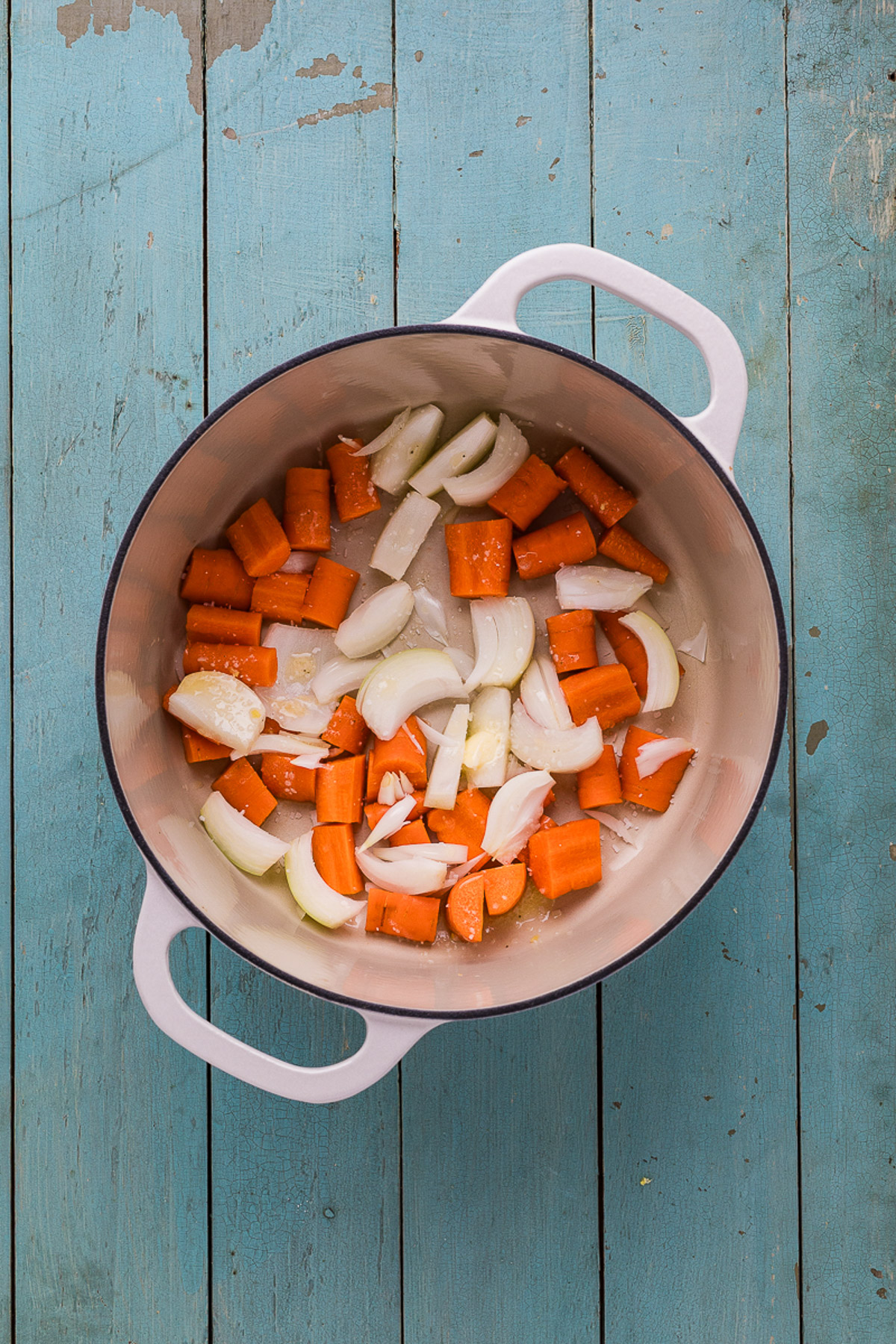 Carrots and onion wedges in the bottom of a dutch oven ready for roasting chicken