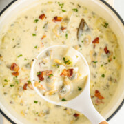 A ladle lifting some New England clam chowder from a pot of more.