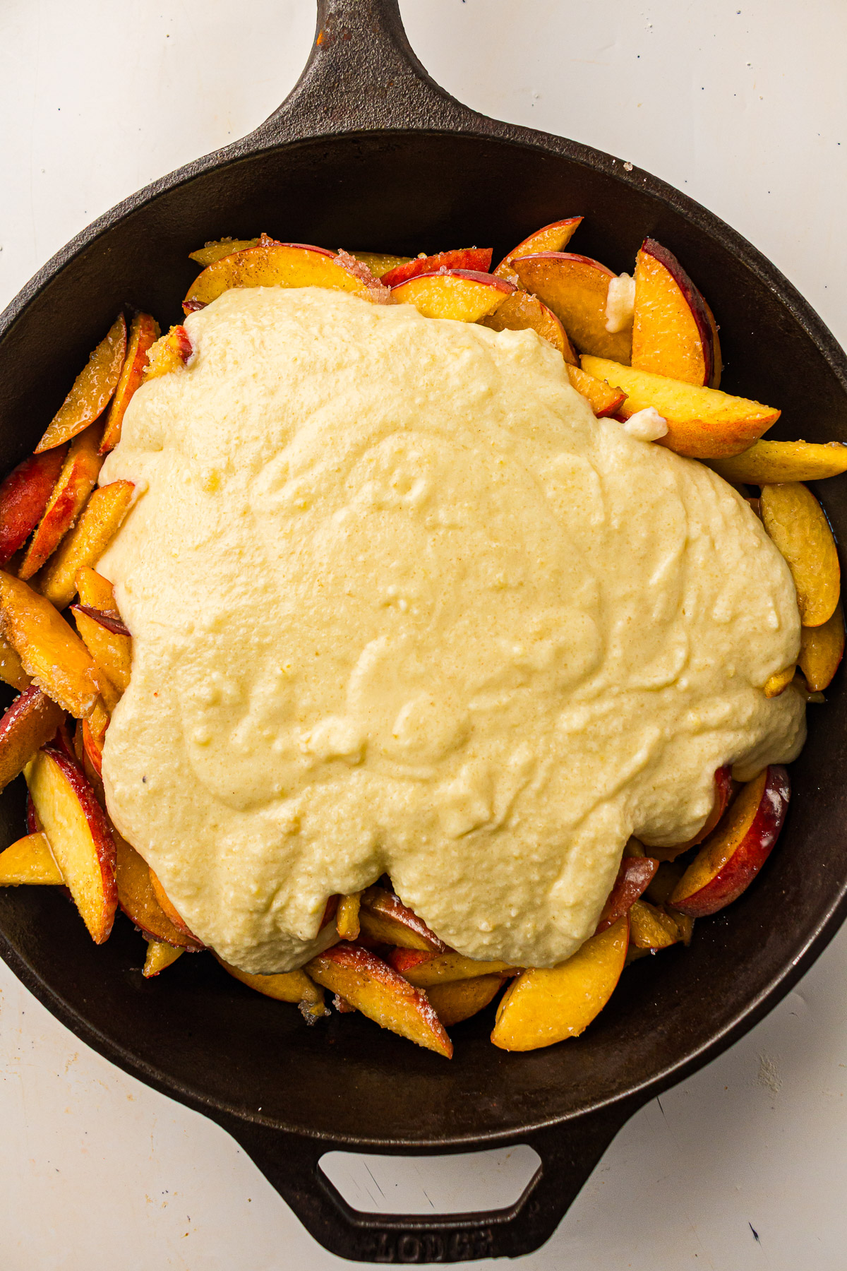 Lightly grease the bottom of your Dutch oven, pour in the peach filling, and spread it into an even layer. Pour the topping batter evenly over the peaches.
