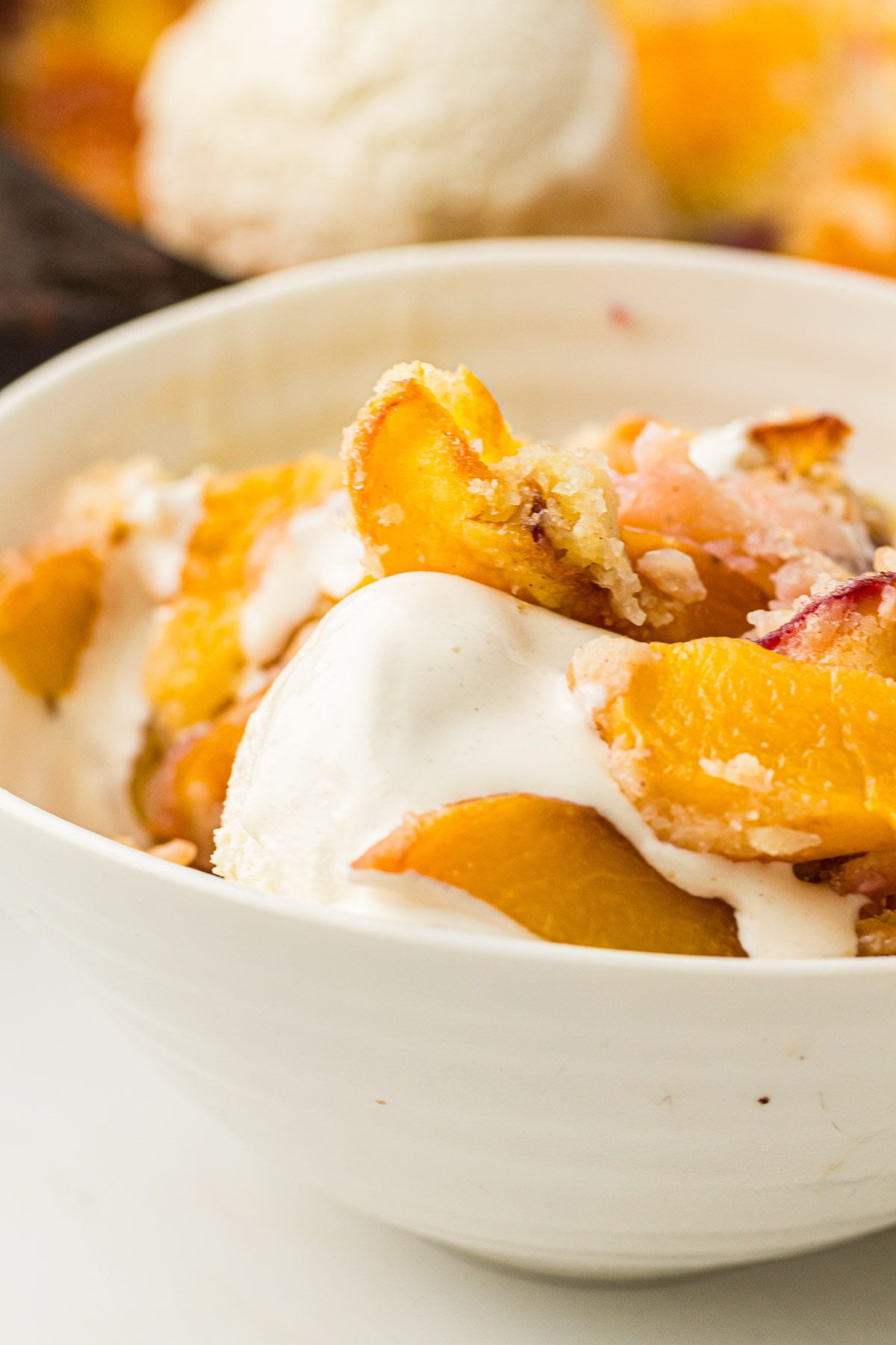 Dutch Oven Peach Cobbler served with ice cream in a white bowl.