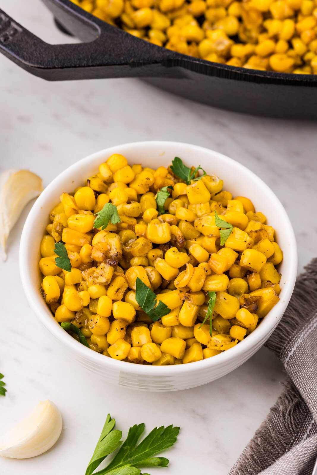Garlic butter skillet corn served in a white bowl garnished with fresh parsley with a cast iron skillet in the background
