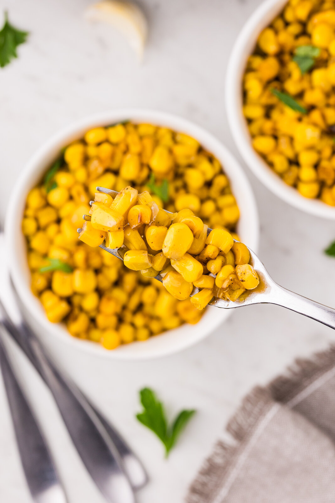 A forkful of garlic butter skillet corn lifted from a white serving bowl
