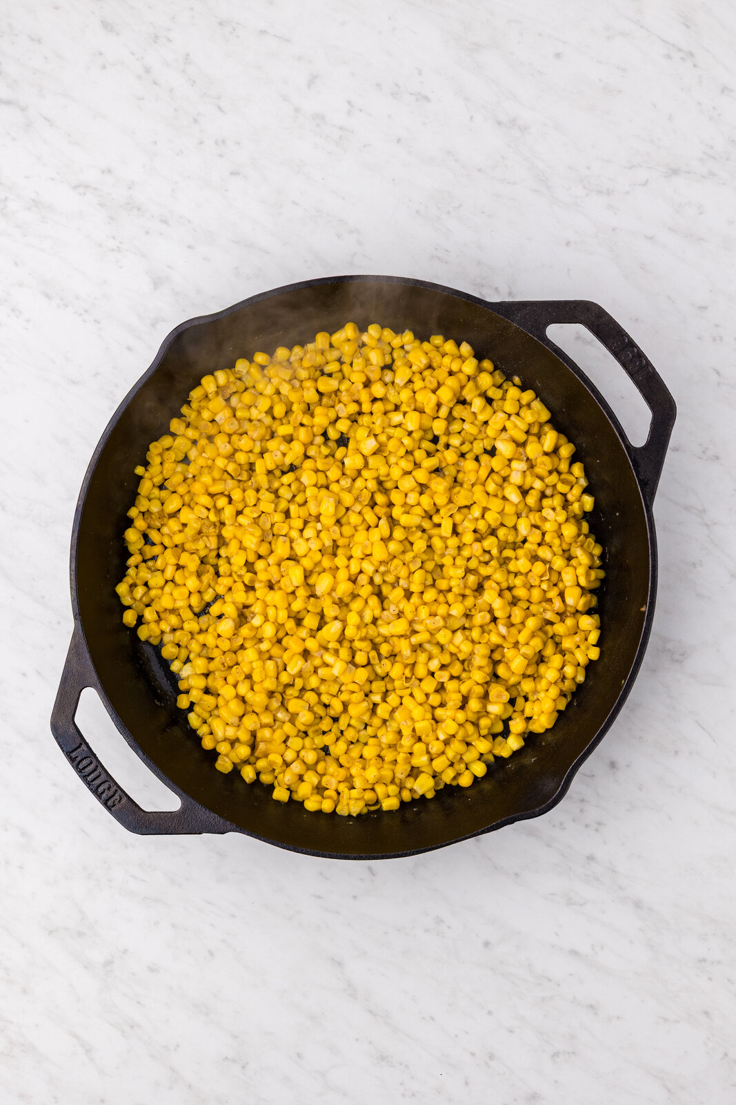 Drained corn kernels added to the garlic butter in a cast iron skillet