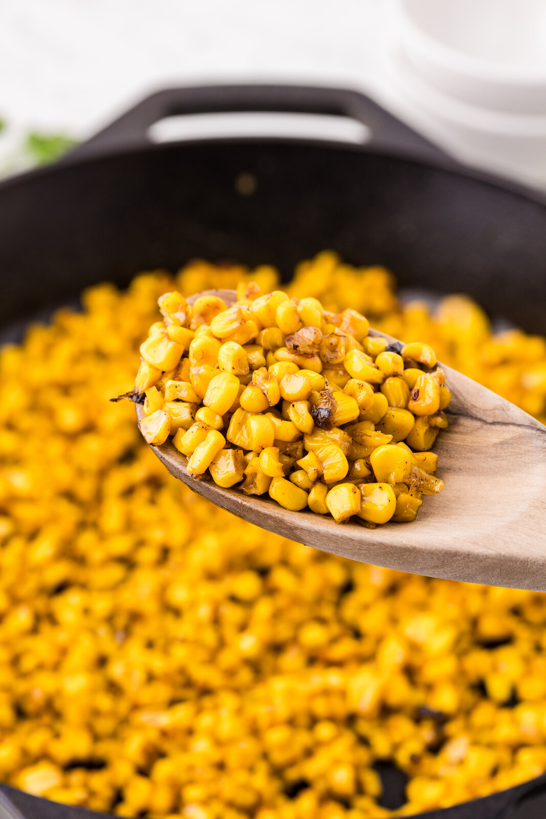 A wooden spoon scooping golden garlic butter skillet corn from a cast iron skillet