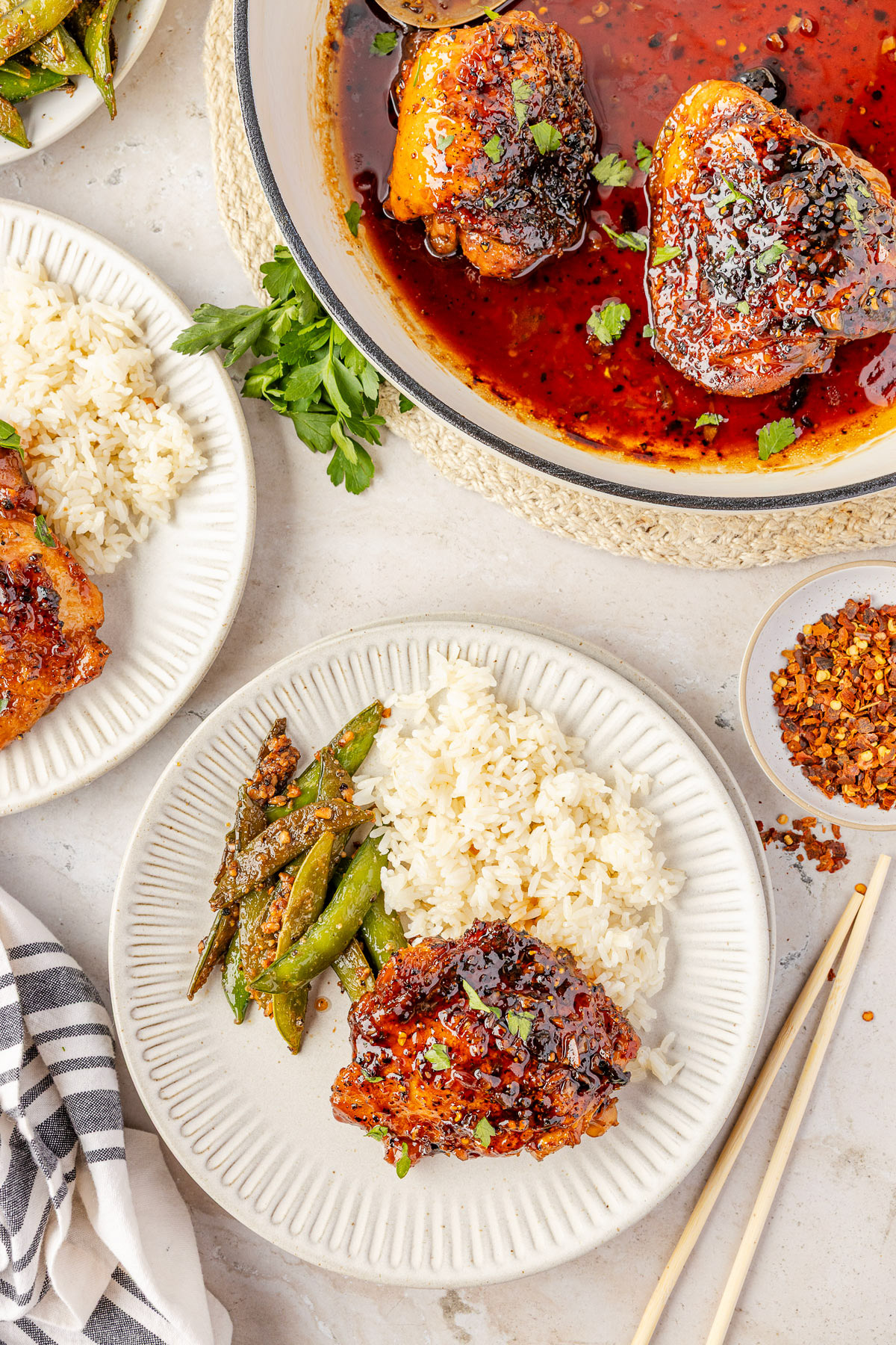 Honey garlic chicken thighs on a plate with rice and sugar snap peas. 