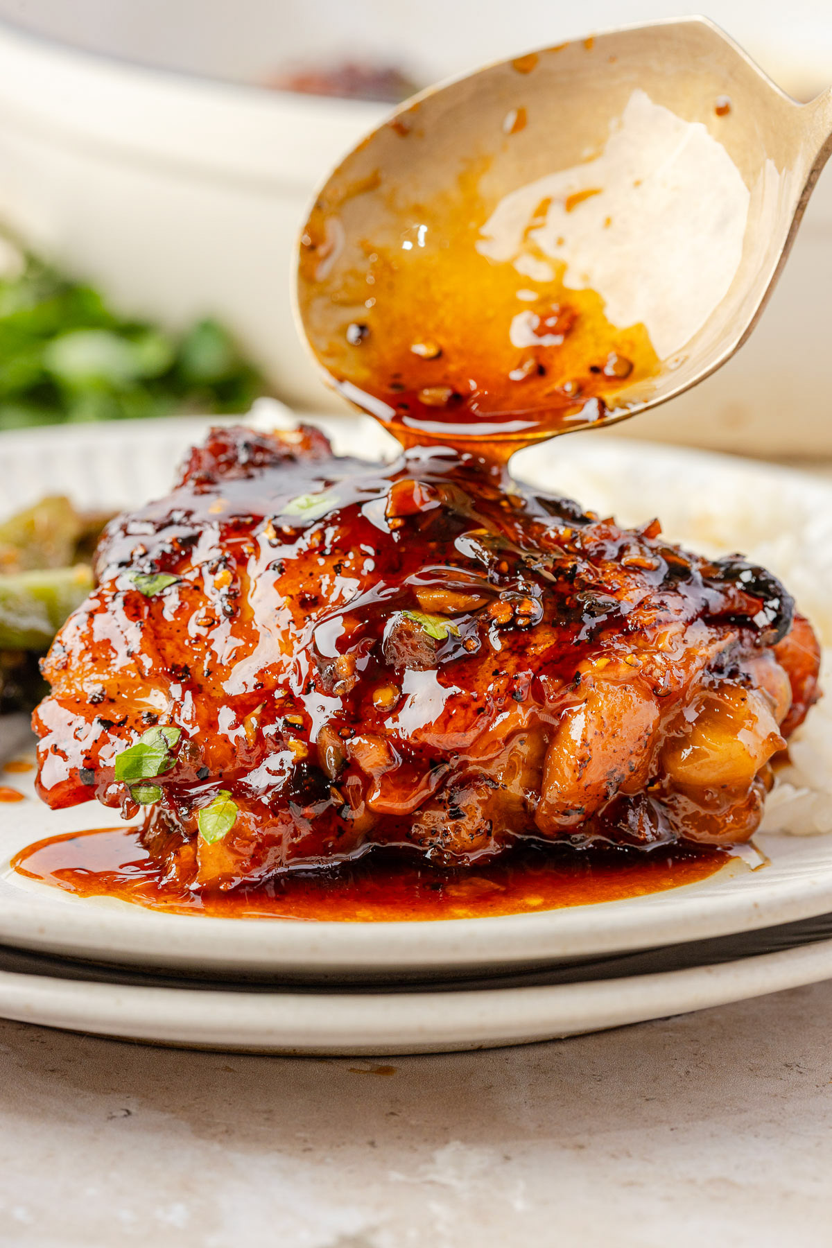 A spoon pouring honey garlic sauce over a chicken thigh.