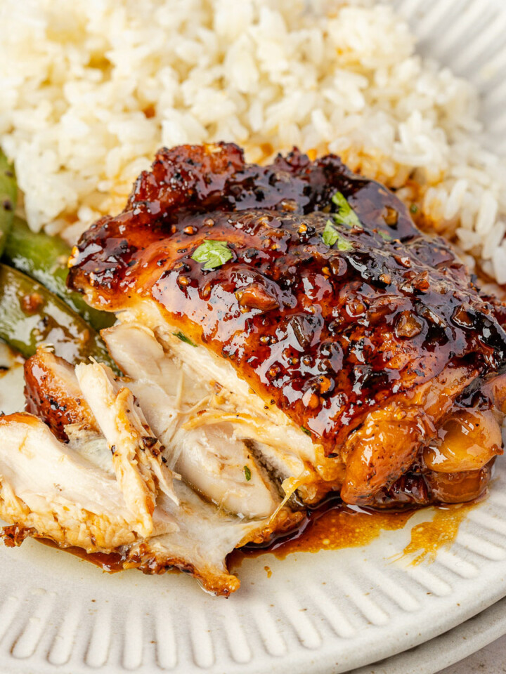 A piece of honey garlic chicken thighs on a plate with a few pieces cut.