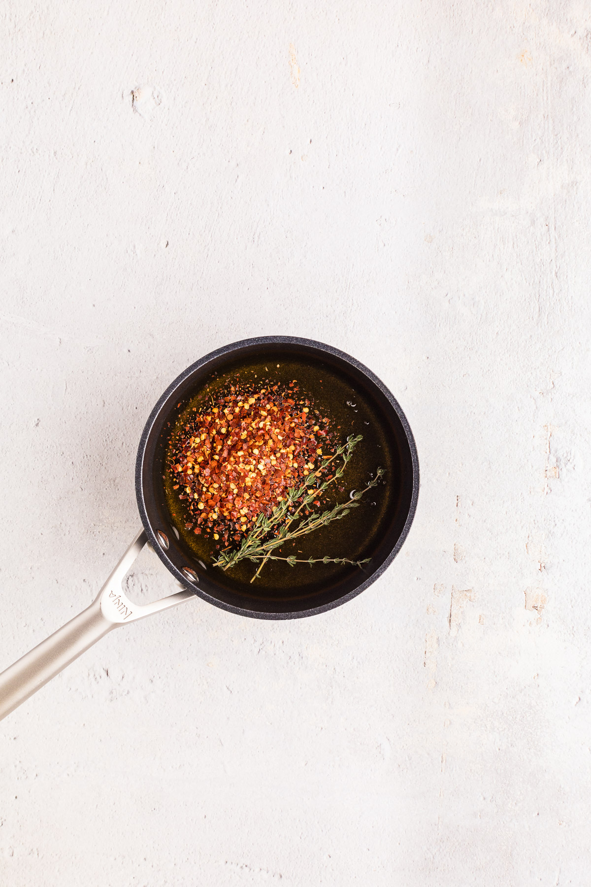 Honey red pepper flakes and fresh thyme in a small pot for hot honey recipe
