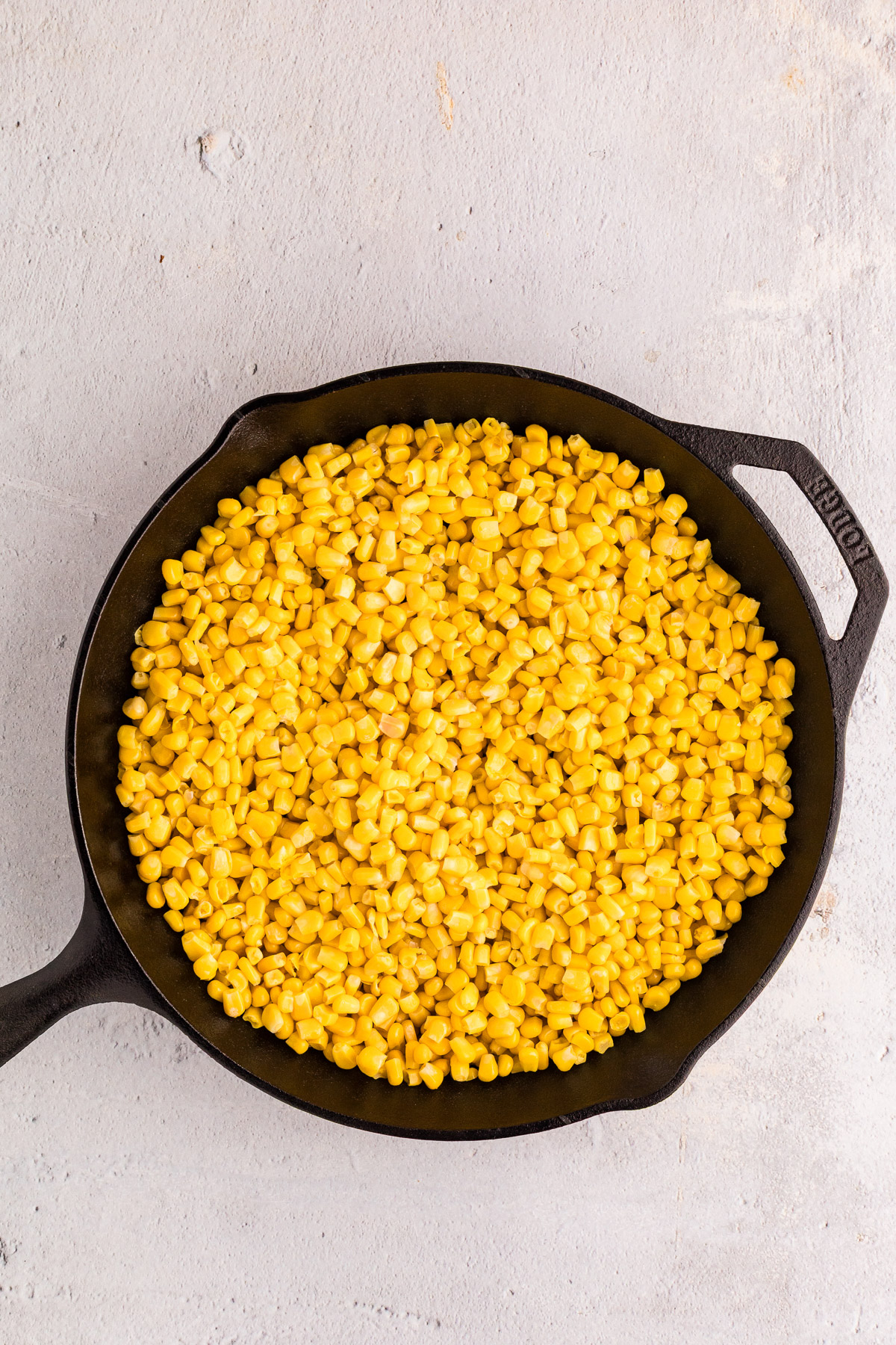 Thawed sweet corn spread in a cast iron skillet ready to char for hot honey butter skillet corn.