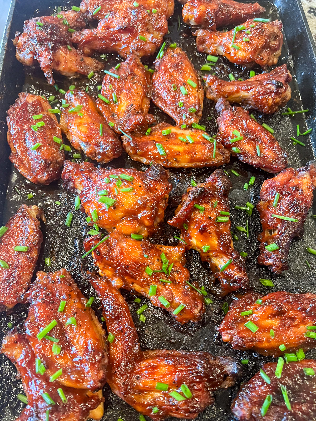 Smoked maple bourbon chicken wings on a flat cast iron skillet garnished with parsley.