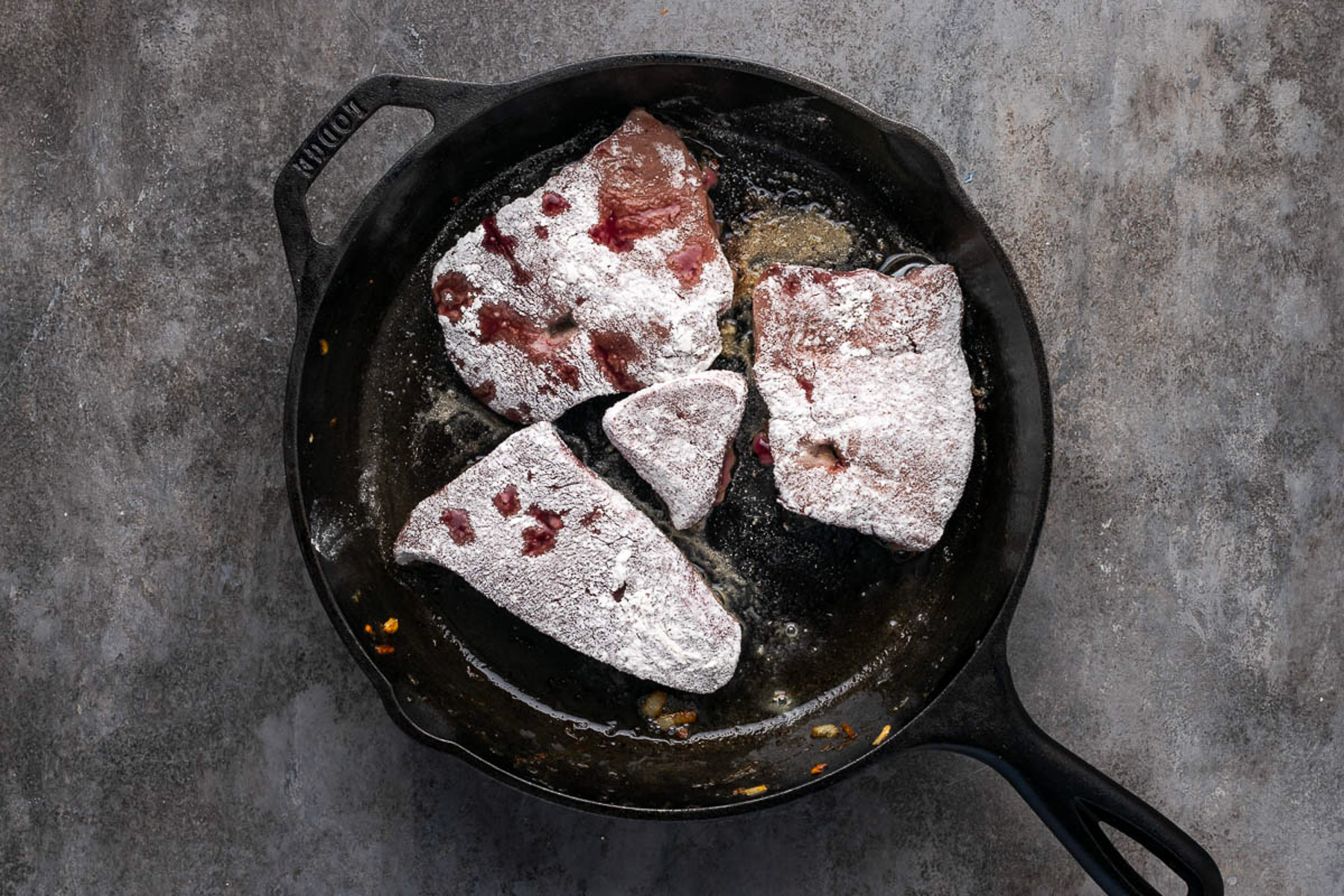Flour-coated beef liver searing in a cast iron skillet