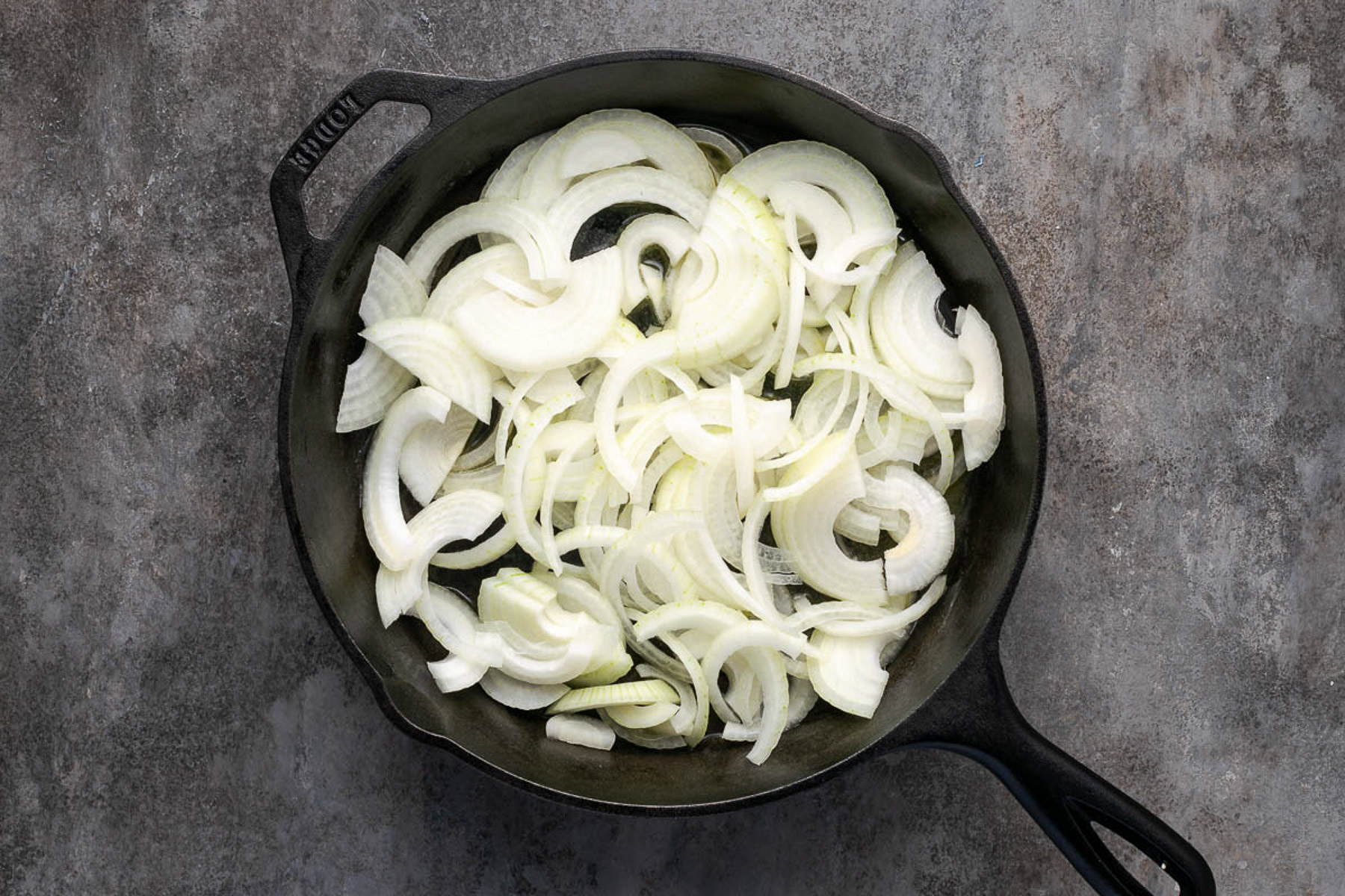 Sliced onions in a cast iron skillet ready to cook