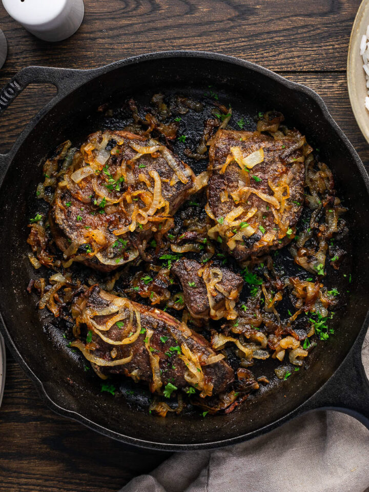 Old fashioned liver and onions in a cast iron skillet with rice bowl and plates on a dark wood table