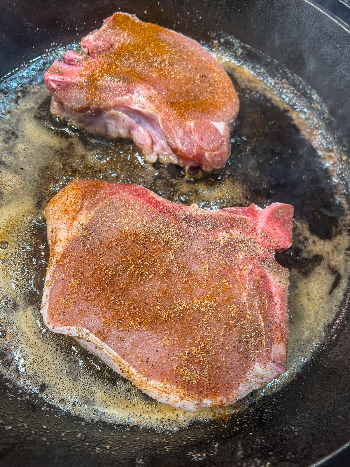 Two seasoned pork chops being seared in a cast iron skillet.