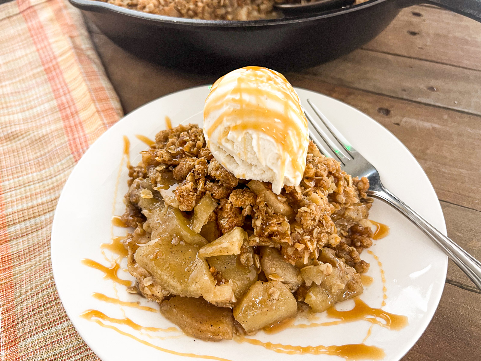 Side view of skillet apple crisp in cast iron with vanilla ice cream melting on top