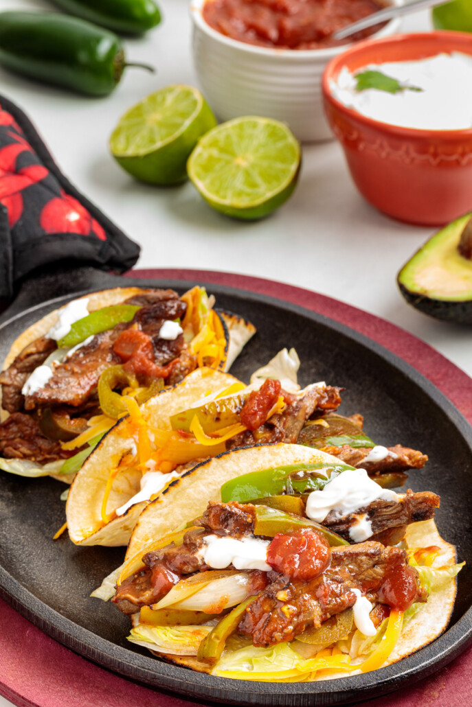 Skillet Fajitas in a cast iron serving pan with all the toppings on the table.