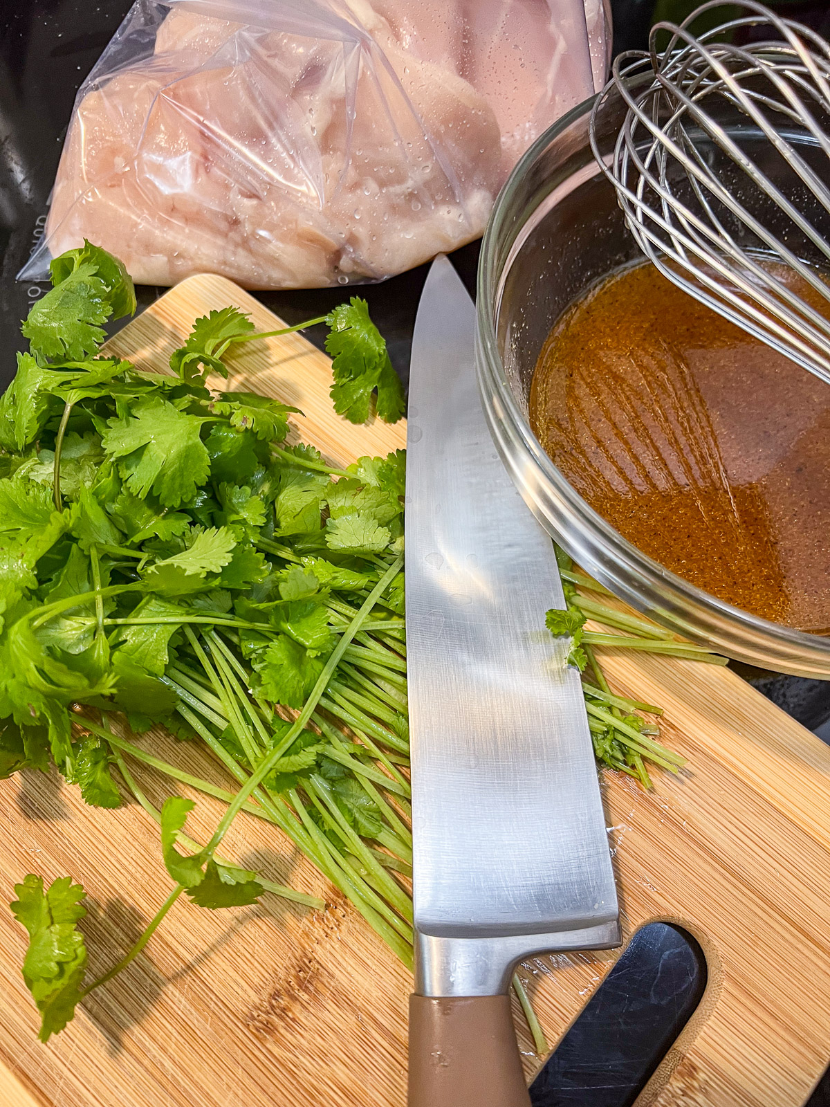 Tequila lime chicken marinade ingredients in a bowl with a wire whisk next to fresh cilantro and chicken in a zip-seal bag