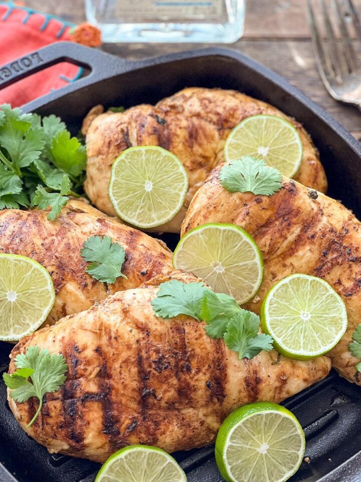 Tequila lime chicken with grill marks in a Lodge cast iron grill pan garnished with lime slices and cilantro