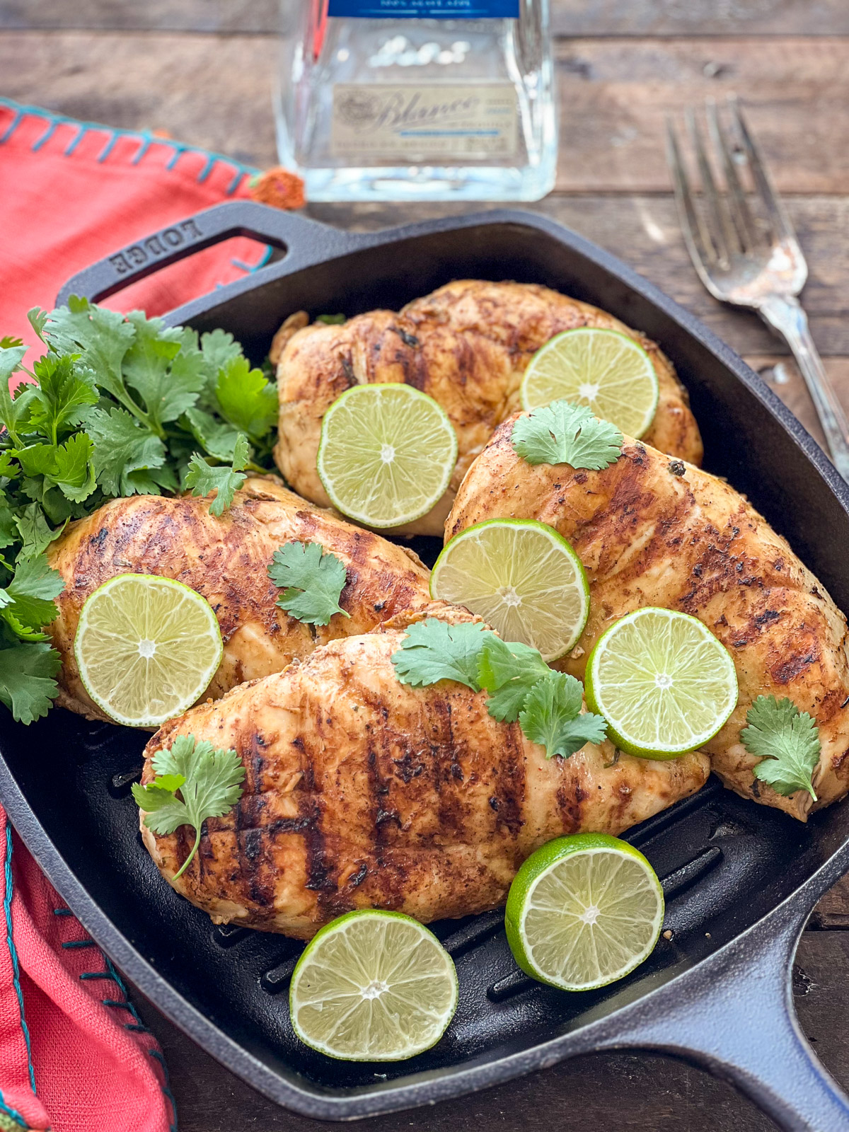 Overhead view of tequila lime chicken in a Lodge cast iron grill pan with tequila bottle in background