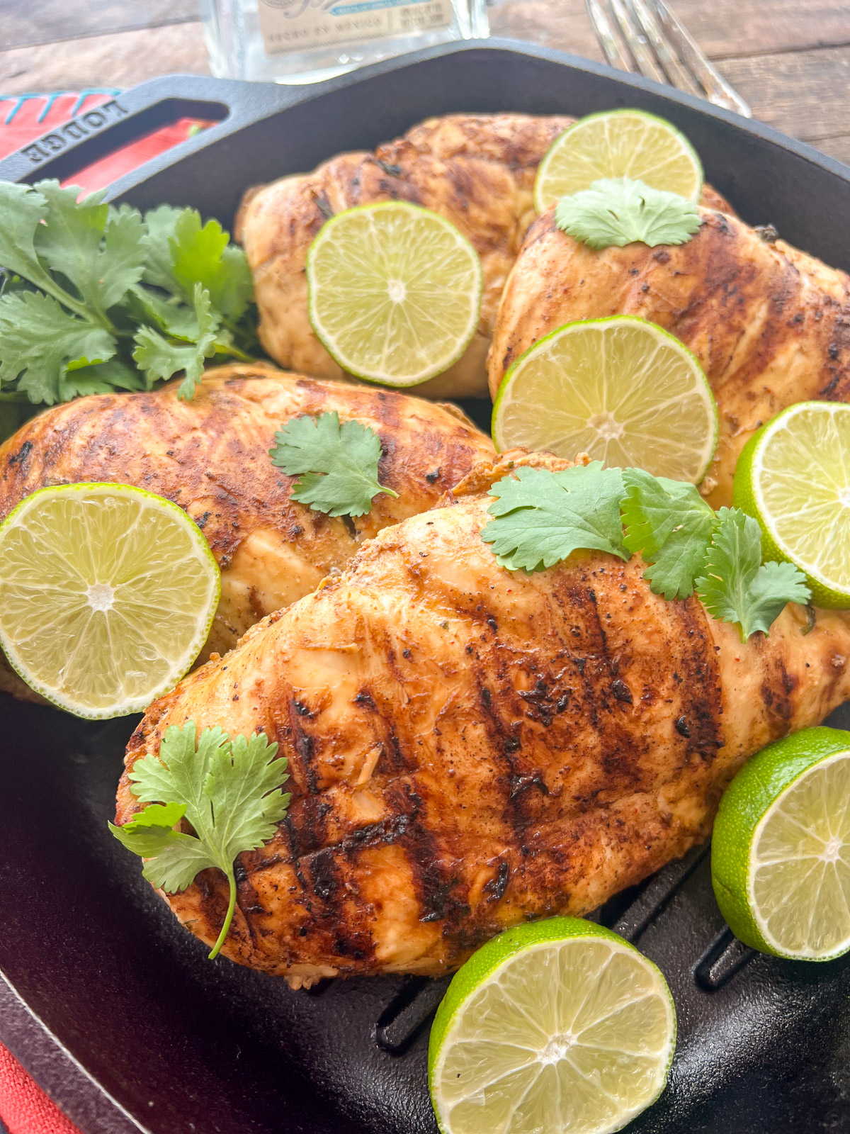 Tequila lime chicken with char marks garnished with lime slices and cilantro in a Lodge cast iron grill pan