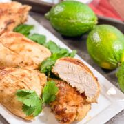 Plated tequila lime chicken on a white platter with one breast sliced open showing juicy interior