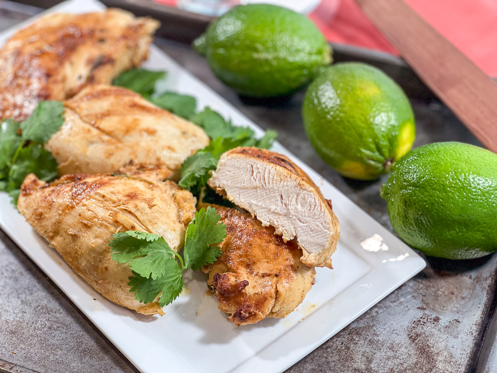 Sliced tequila lime chicken on a white platter showing juicy interior with fresh cilantro and limes