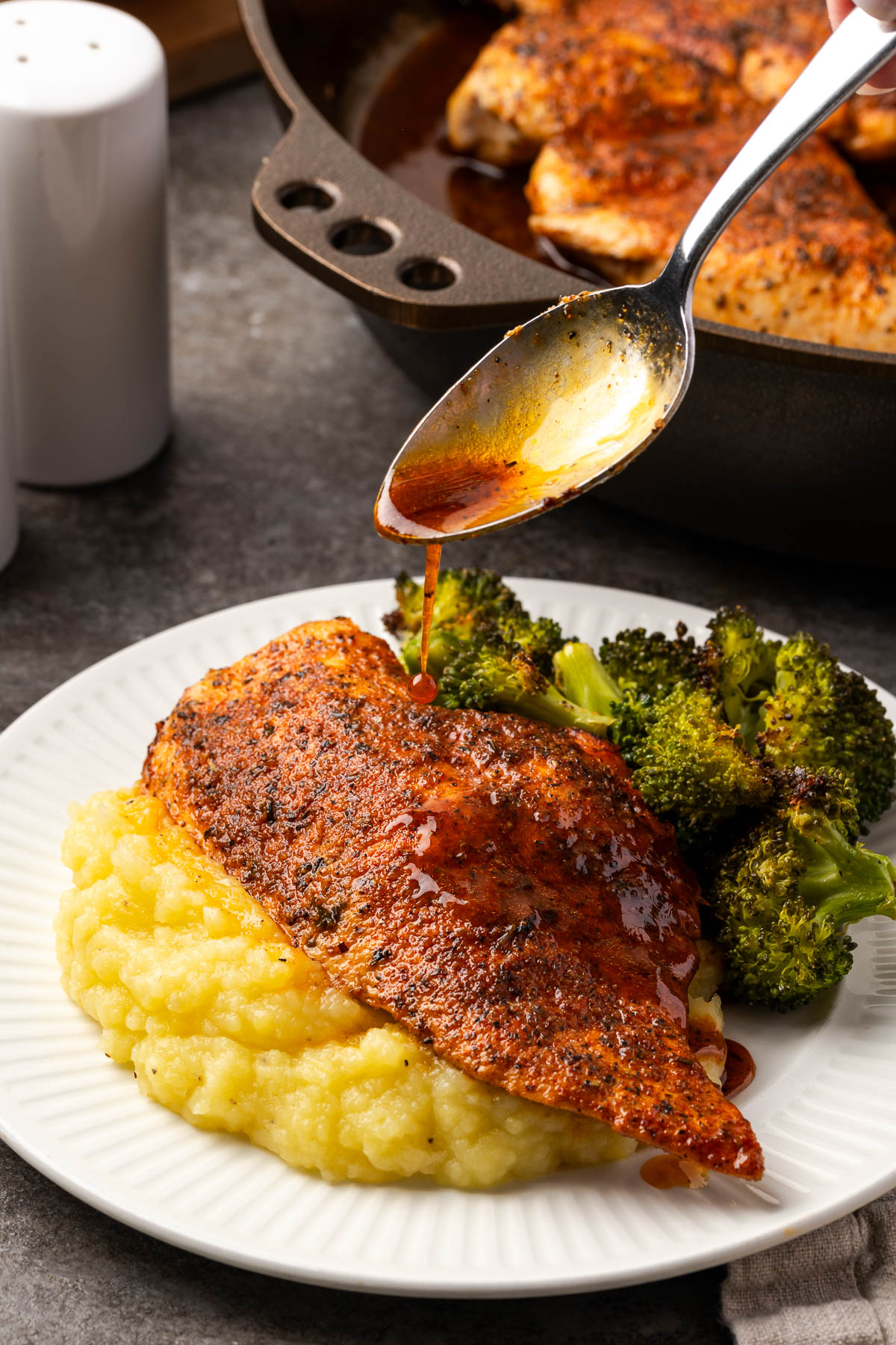 A spoon pouring juice over the a piece of cast iron skillet chicken.