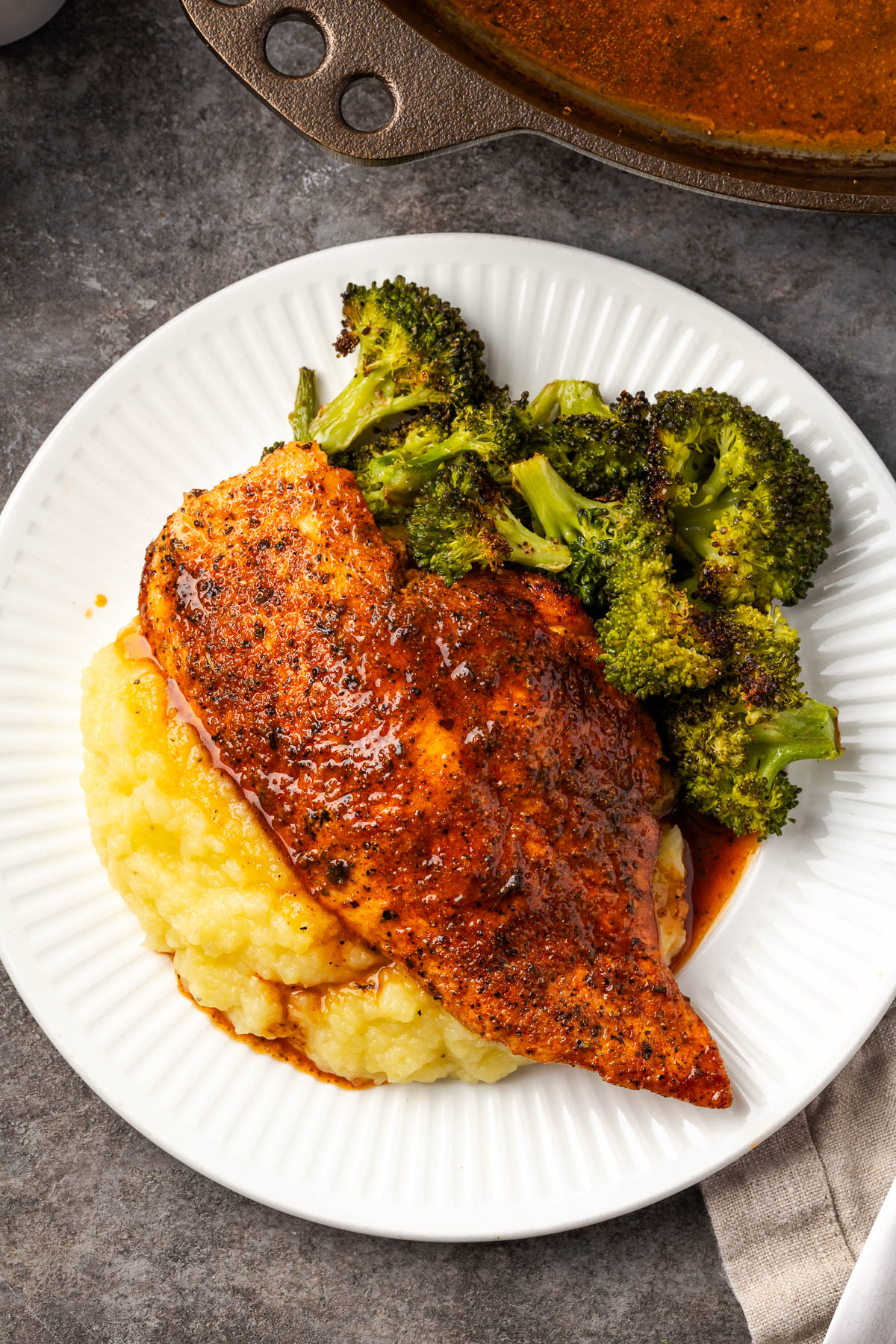 Cast iron skillet chicken served with broccoli and mashed potatoes on a white plate. 